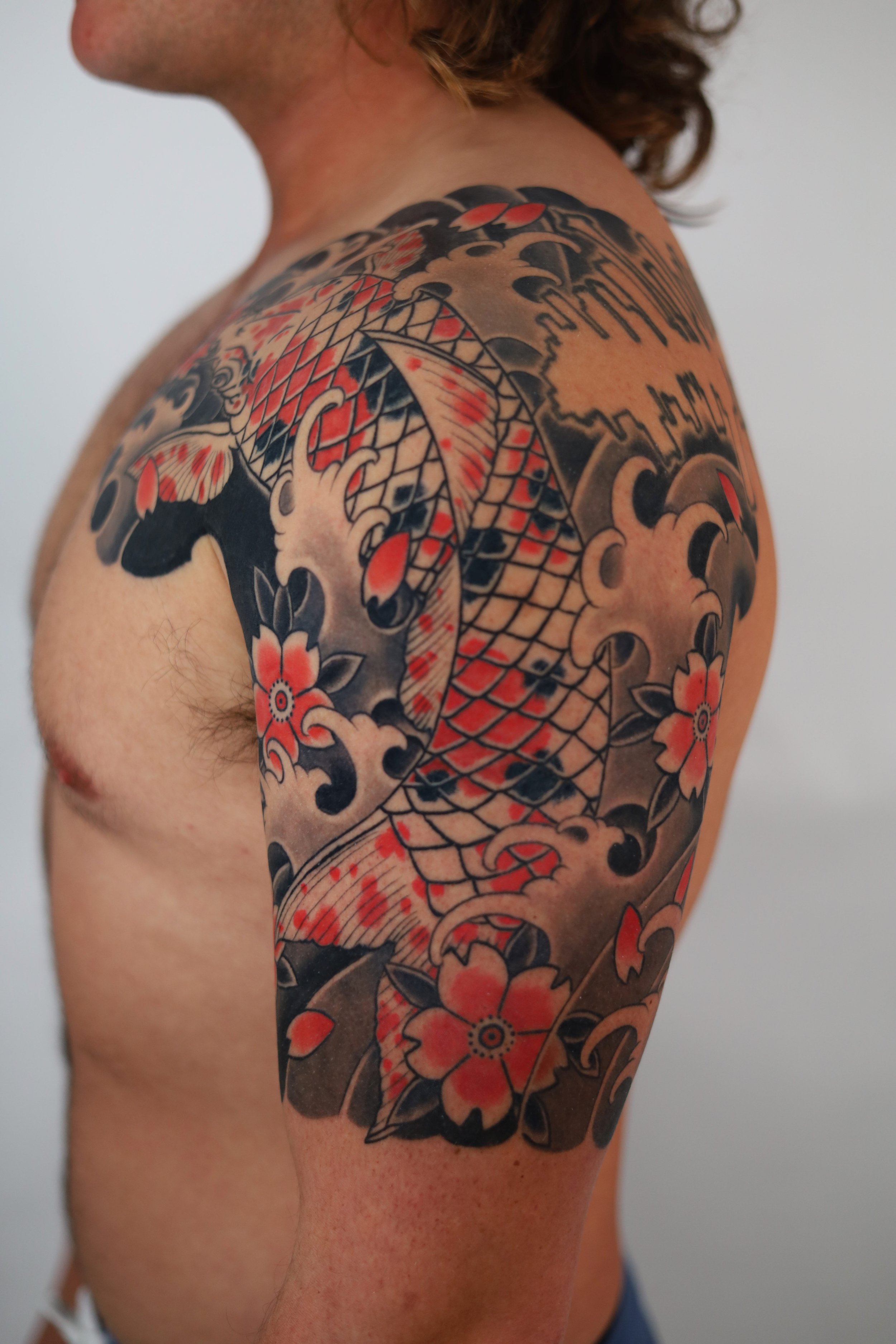 Tattoo of a koi fish with floral and cloud motifs on a man's upper arm and shoulder.