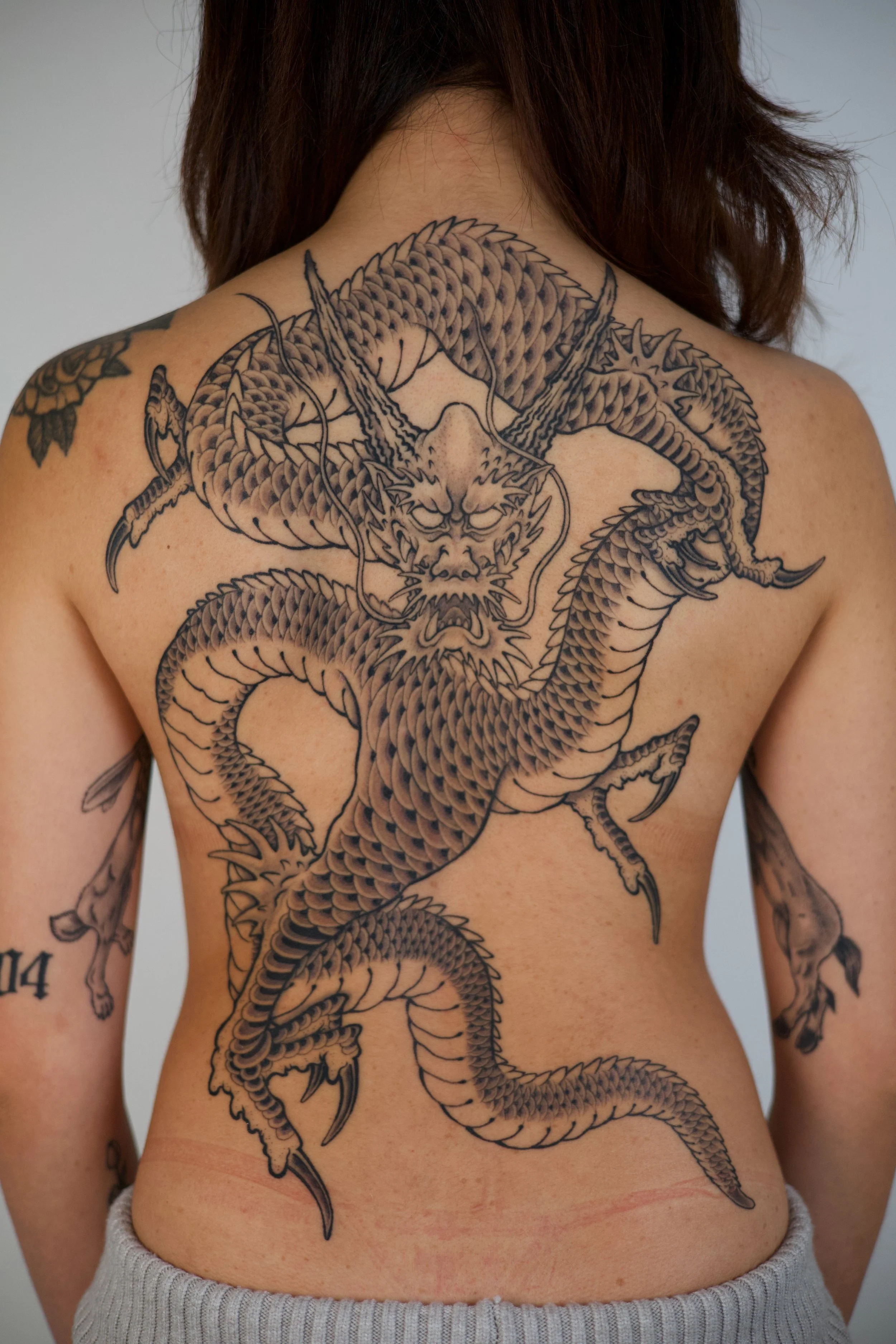 Back tattoo of a detailed black and gray dragon with fierce facial expression.