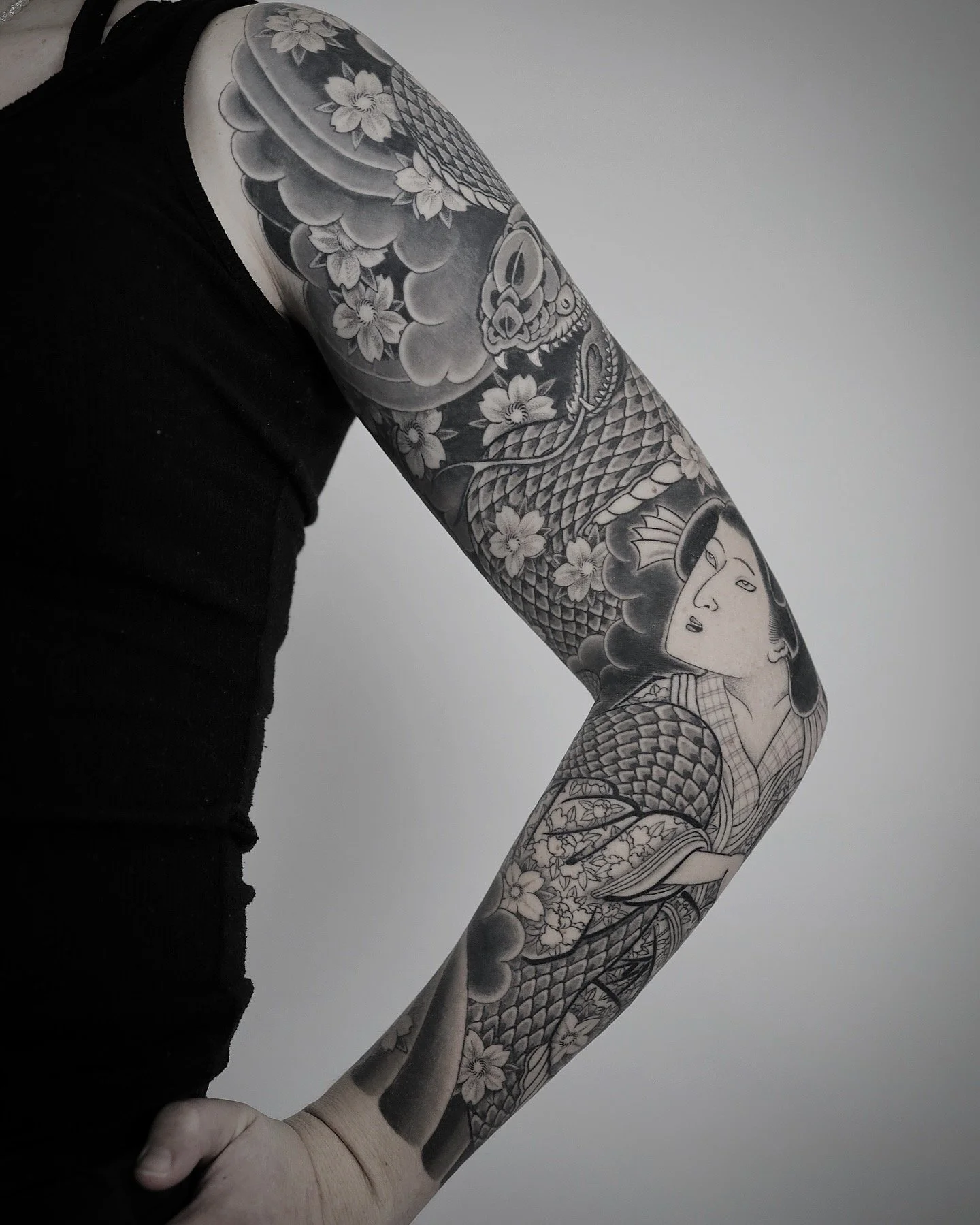 Black and gray tattoo sleeve featuring a traditional Japanese woman, a snake, cherry blossoms, clouds, and a skull.