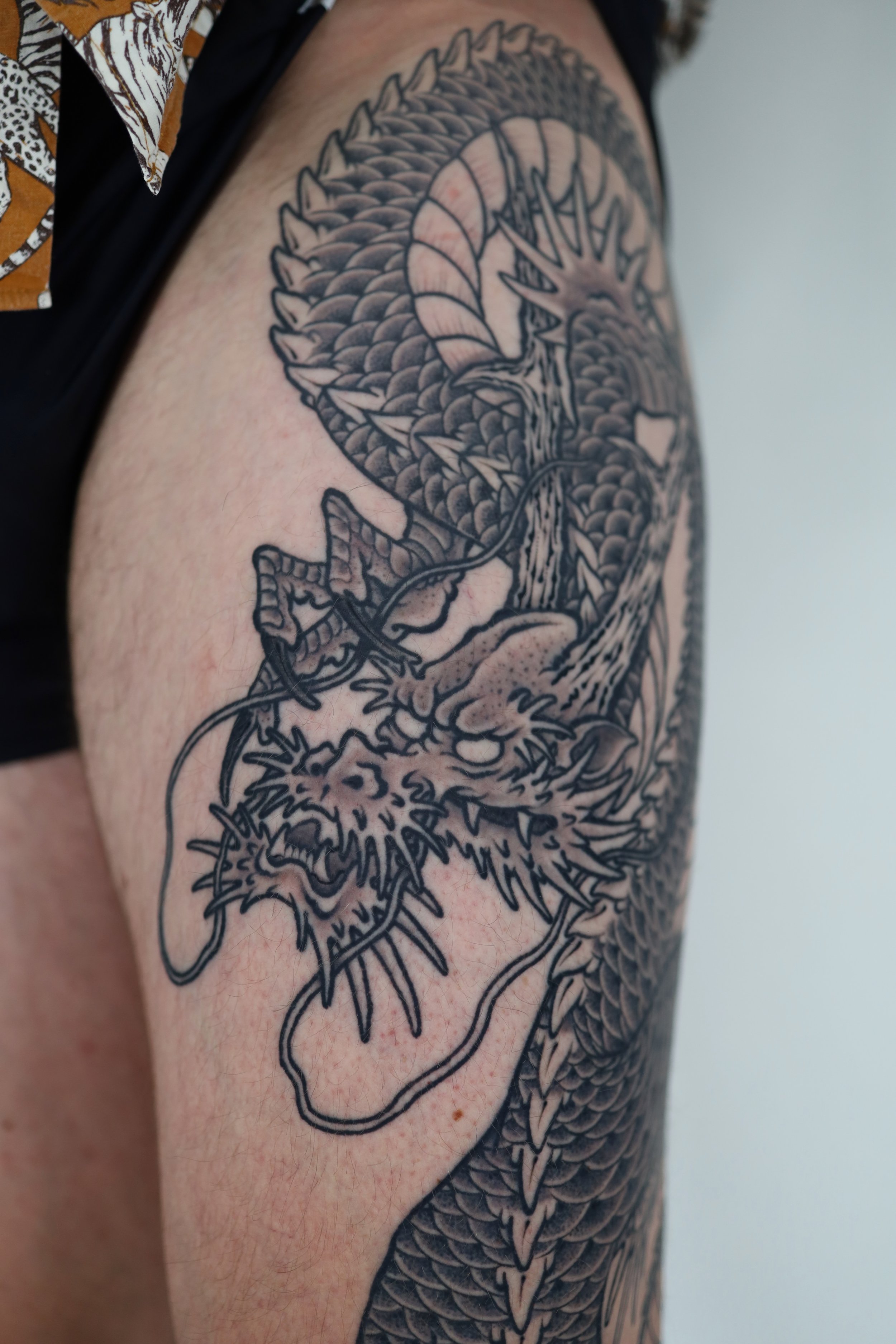 A detailed black and grey tattoo of a dragon's head with scales and sharp features on a person's upper arm.