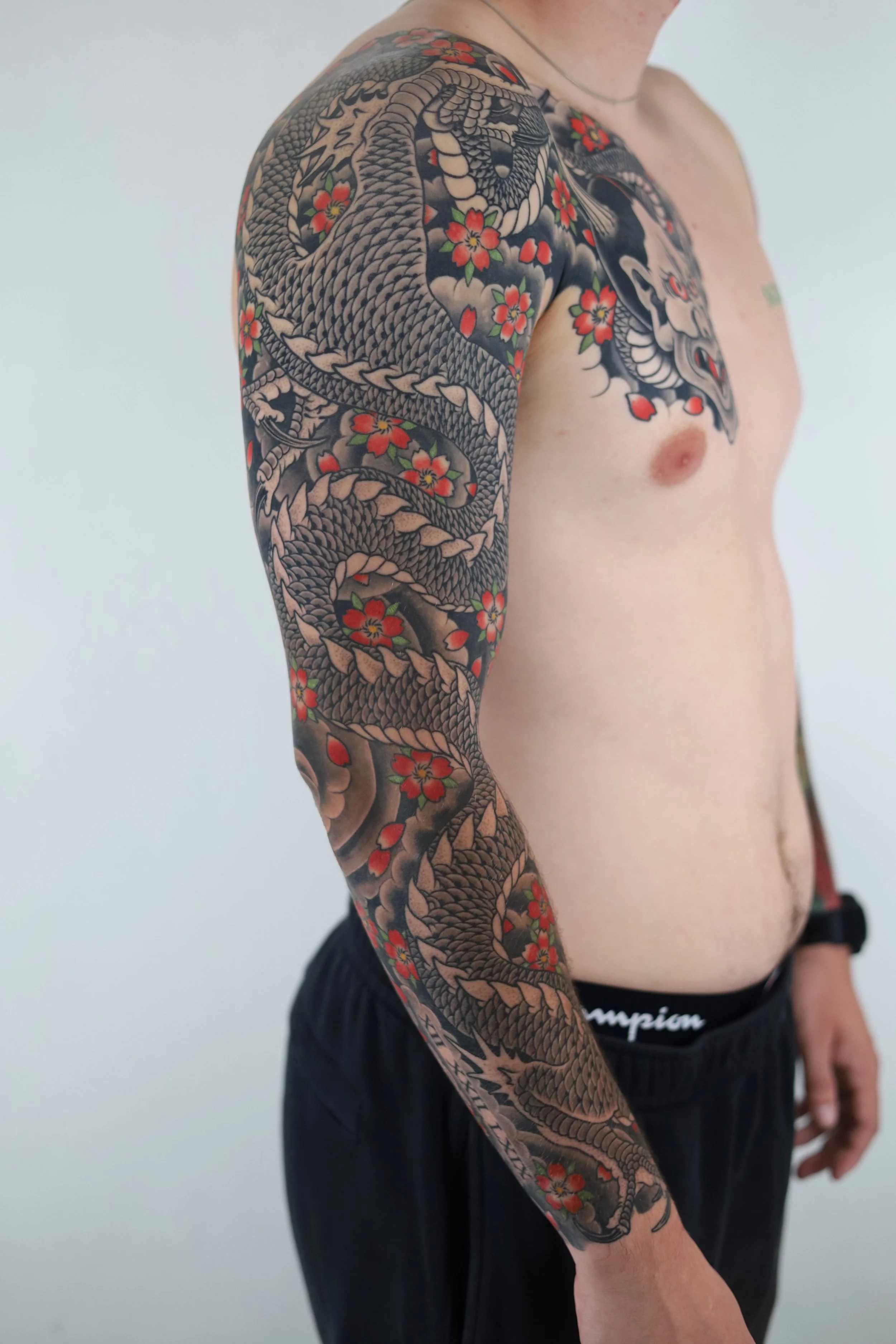 A man with a traditional Japanese-style tattoo of a dragon and cherry blossoms covering his upper arm and shoulder.