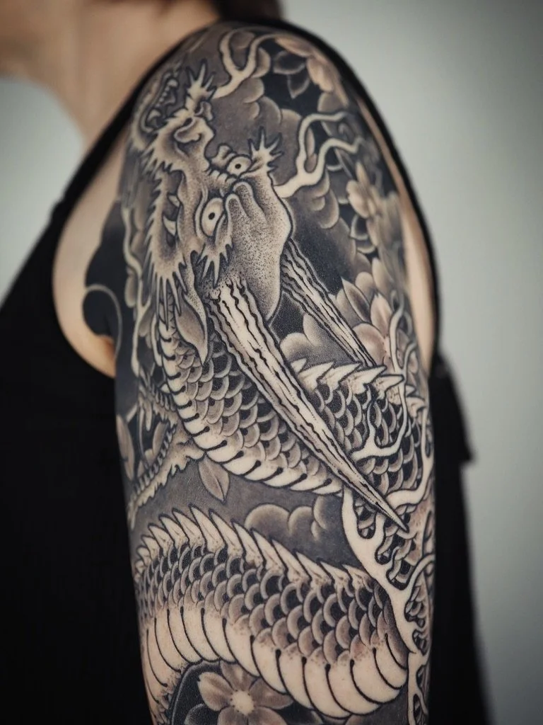 Black and gray tattoo of a dragon on a person's upper arm.