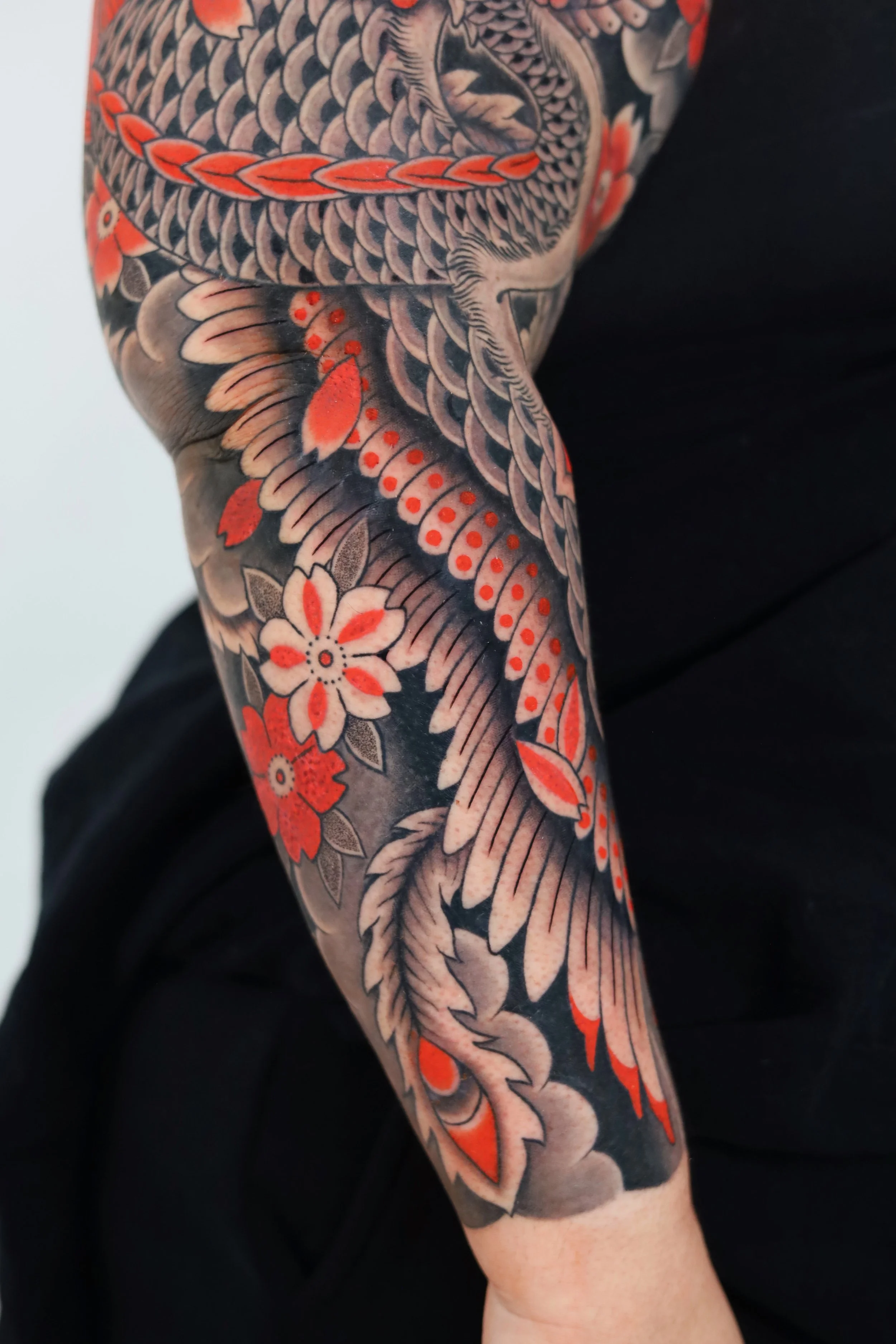 Tattoo sleeve on arm featuring a detailed black and gray dragon intertwined with orange and white flowers.