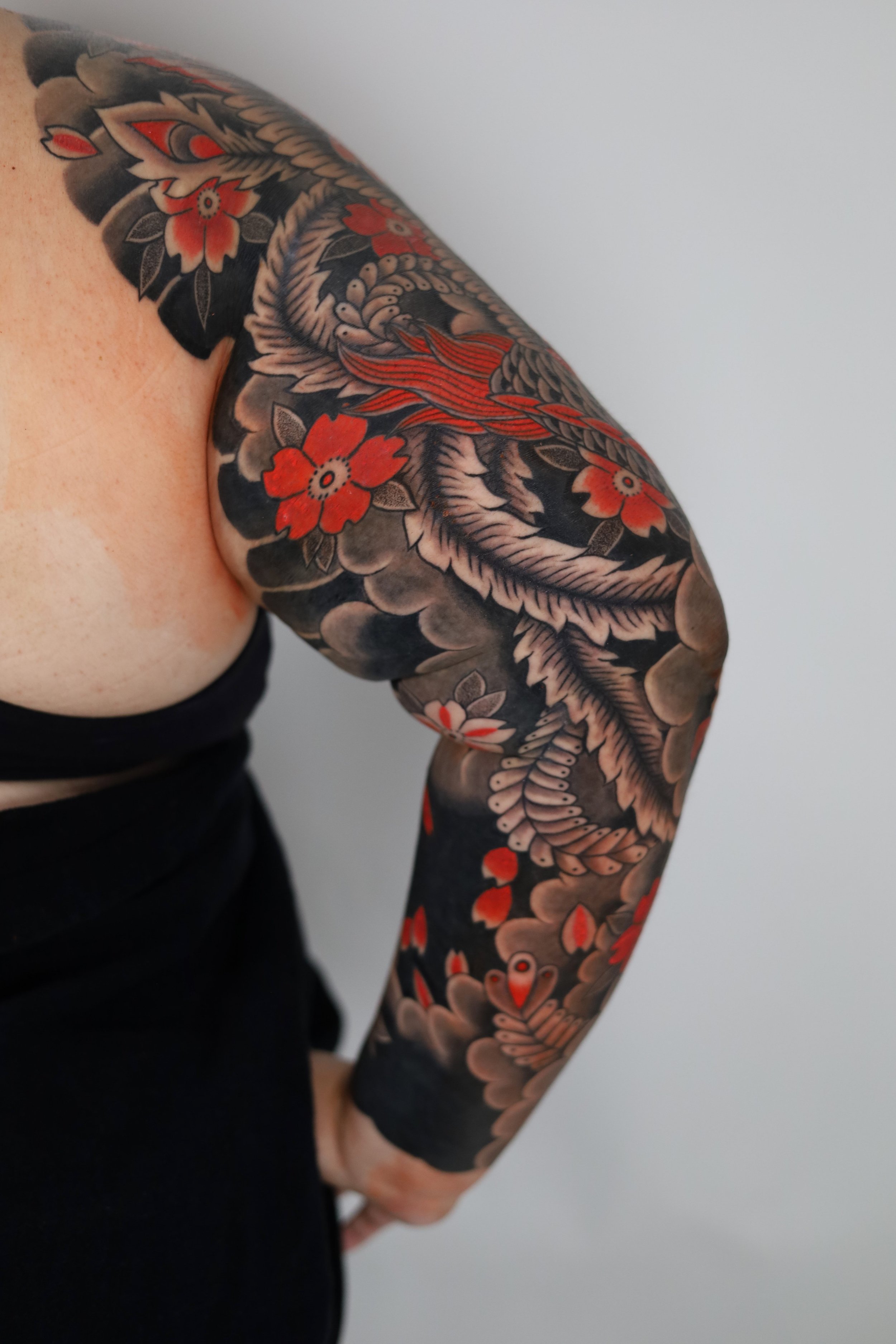 Tattooed arm with a Japanese style dragon, red and black flowers, and clouds.