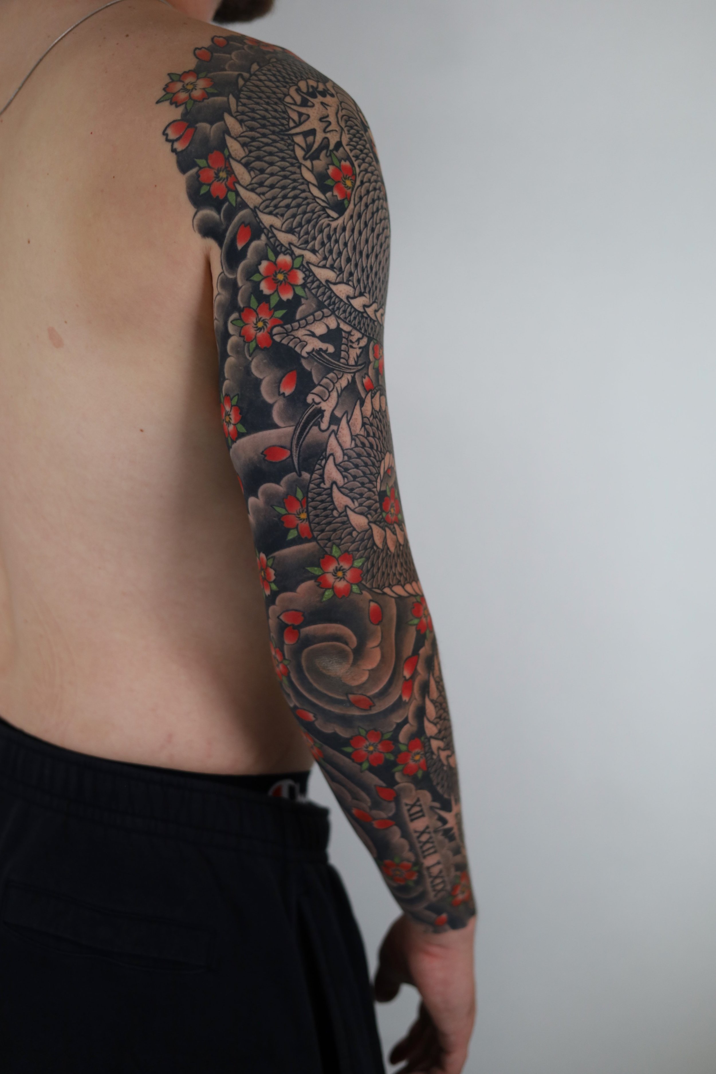 A tattoo of a dragon with red flowers on a person's arm.