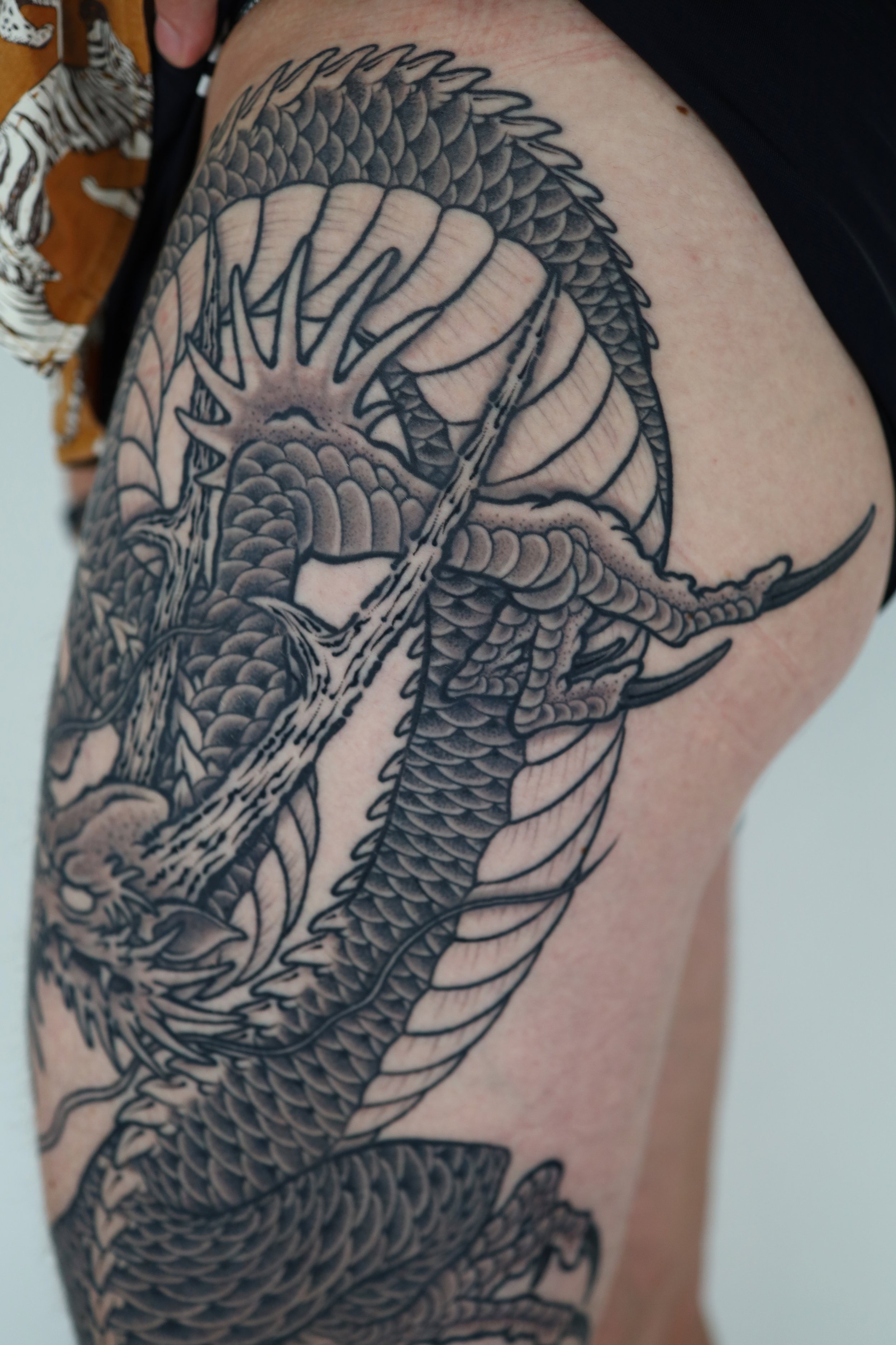 Black and gray tattoo of a dragon wrapping around the upper arm and shoulder.
