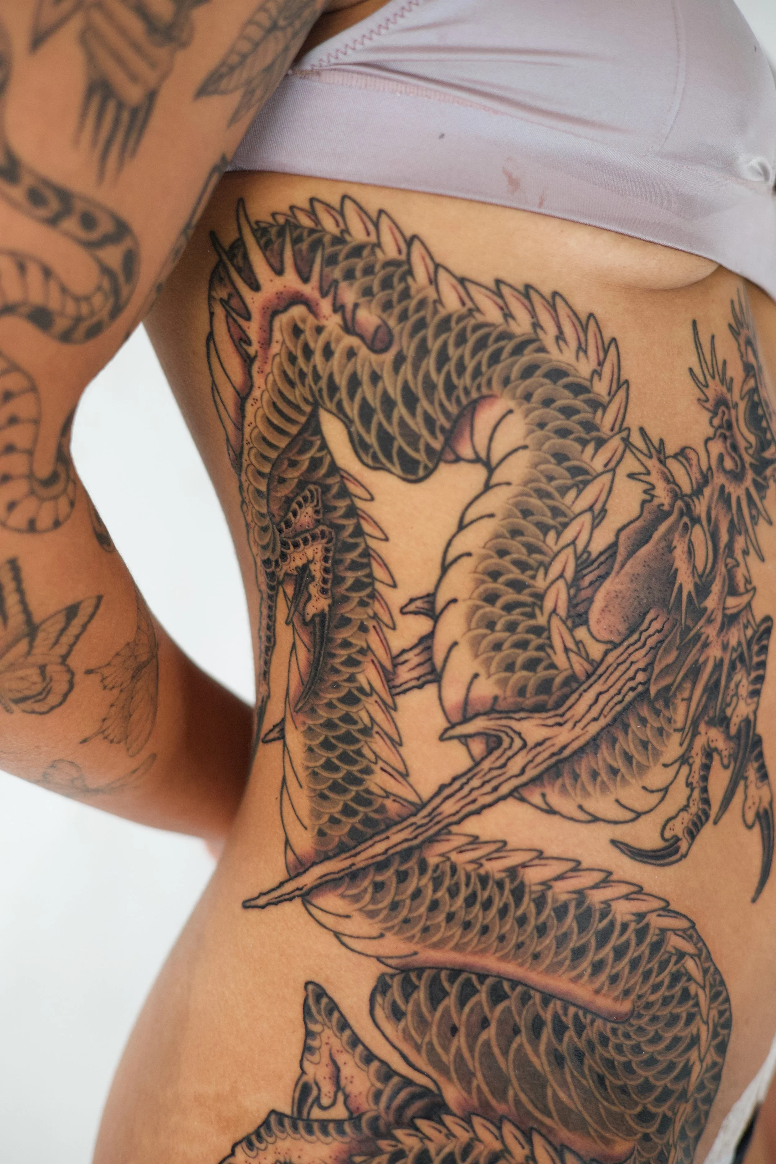 Close-up of a person's torso with a large, intricate dragon tattoo covering the side and ribs, featuring detailed scales, claws, and facial features.