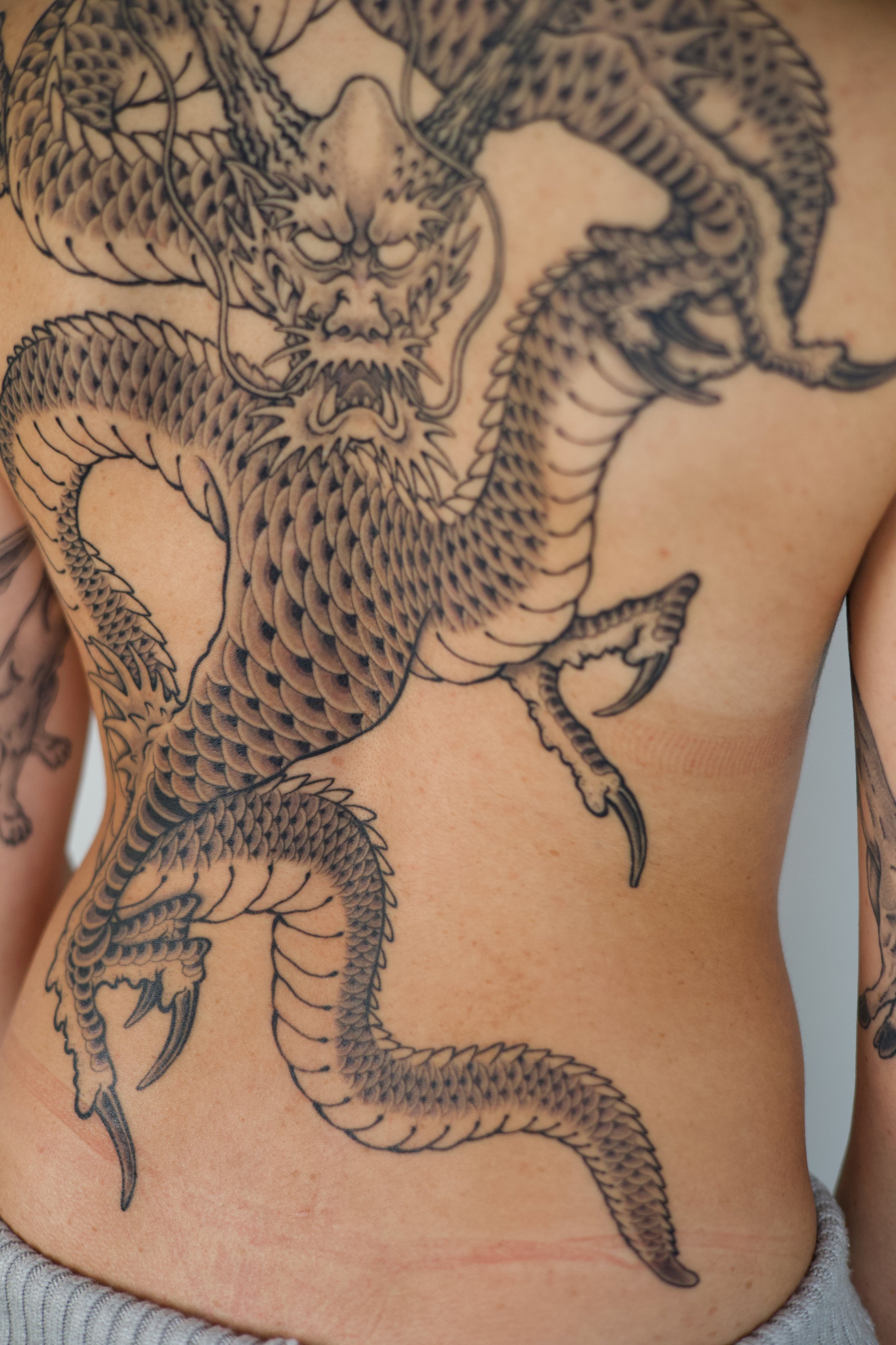 Close-up of a person's upper body showcasing a large black and gray dragon tattoo across the chest, abdomen, and shoulder.