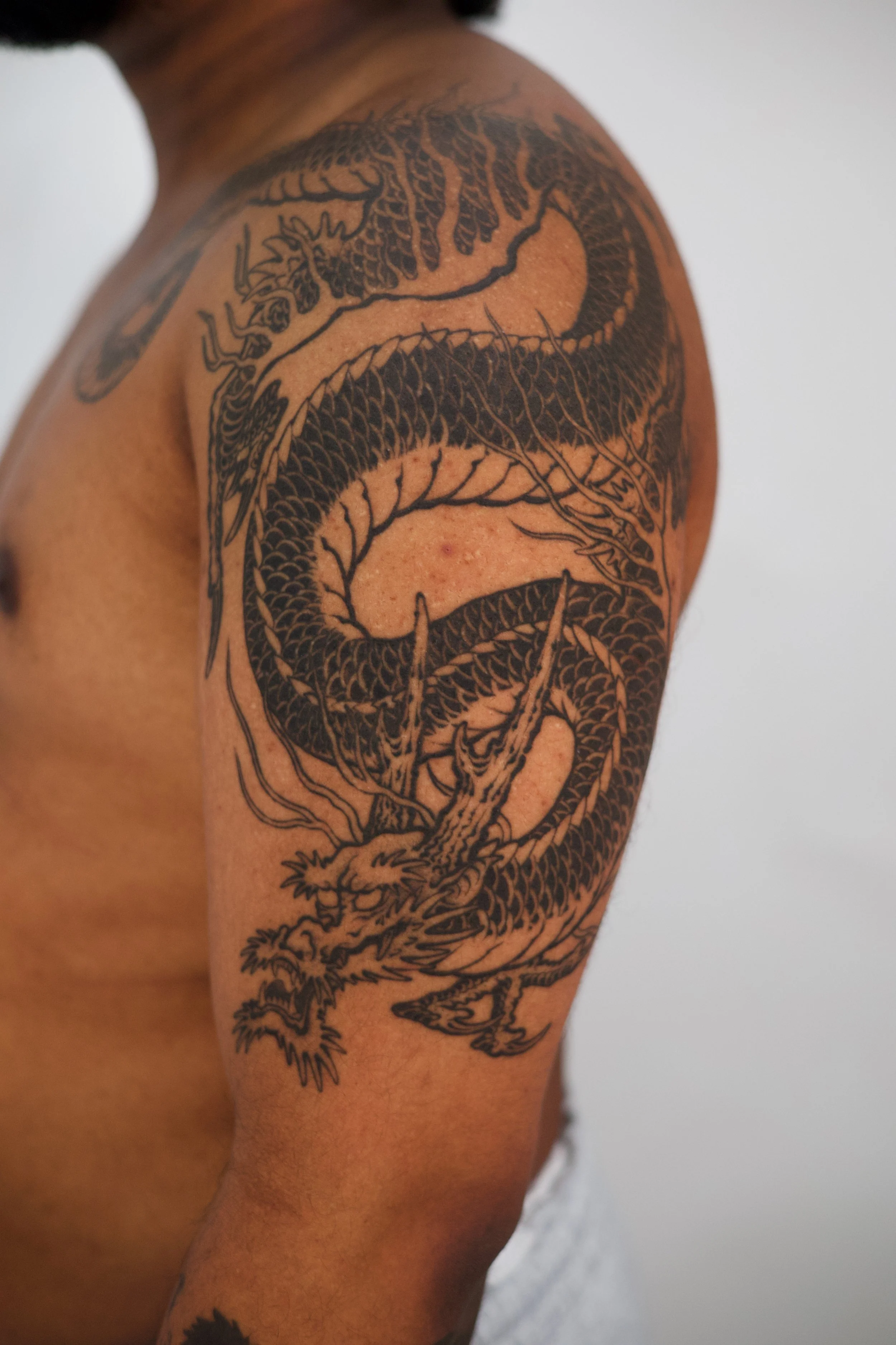 A black tattoo of a dragon on a person's upper arm and shoulder.