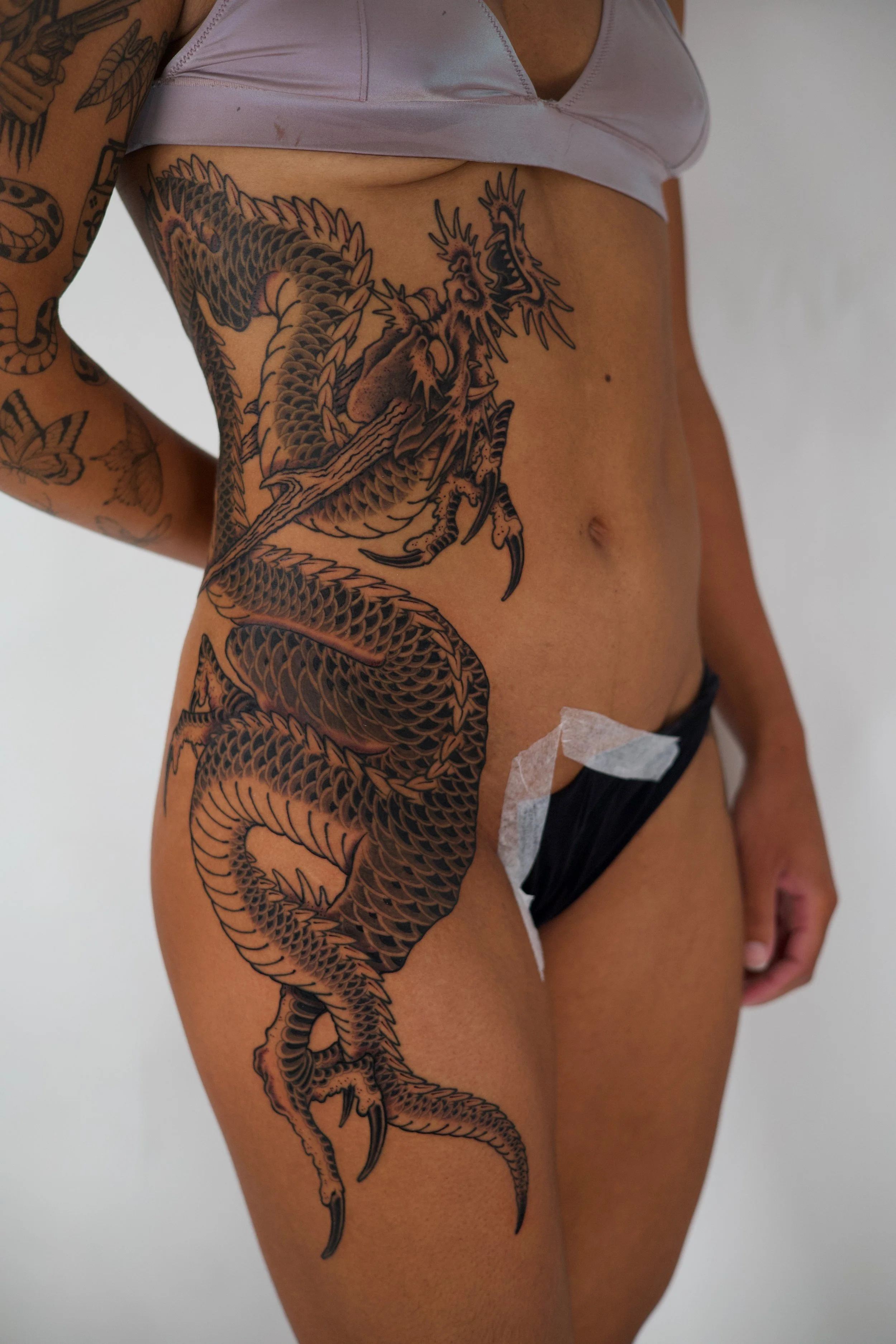Close-up of a person's side and hip showing a large black and gray tattoo of a dragon covering the torso and upper leg.