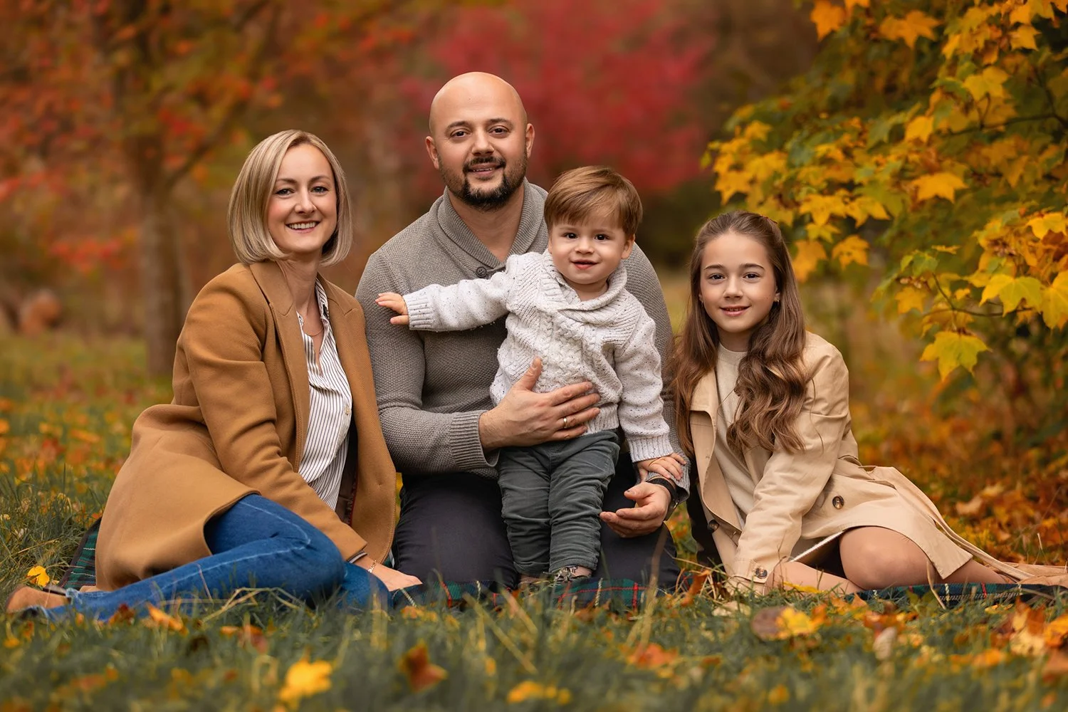 Autumn Mini Sessions 2026: mum, dad and their 2 children sitting on a blanket surrounded by autumn leaves during their family photoshoot in Leeds