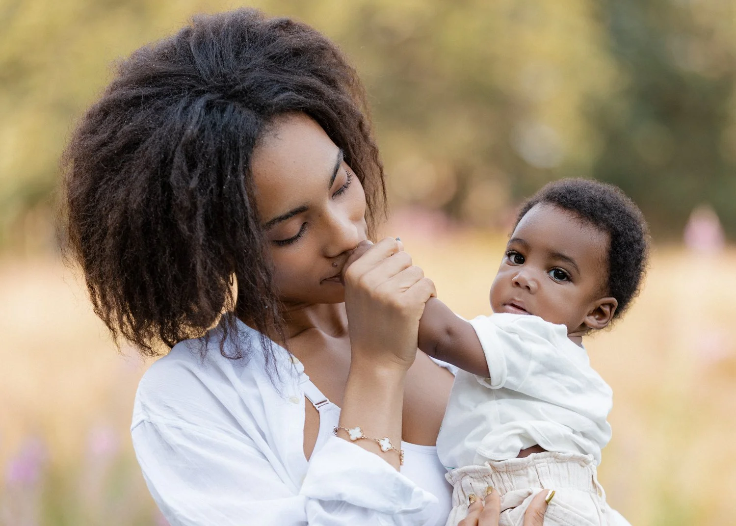 A young mother kissing her baby son's hand on a sunny summer evening in Leeds