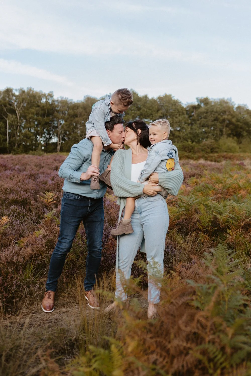 Dad with his son on his shoulders kissing his wife who's holding their youngest son during their family shoot in Leeds