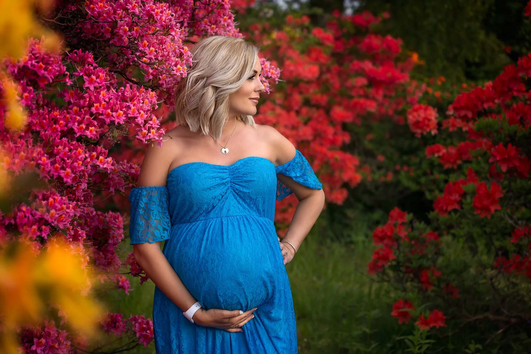 Leeds maternity photography: beautiful blond pregnant woman in a long blue dress surrounded by pink and red flowers. 