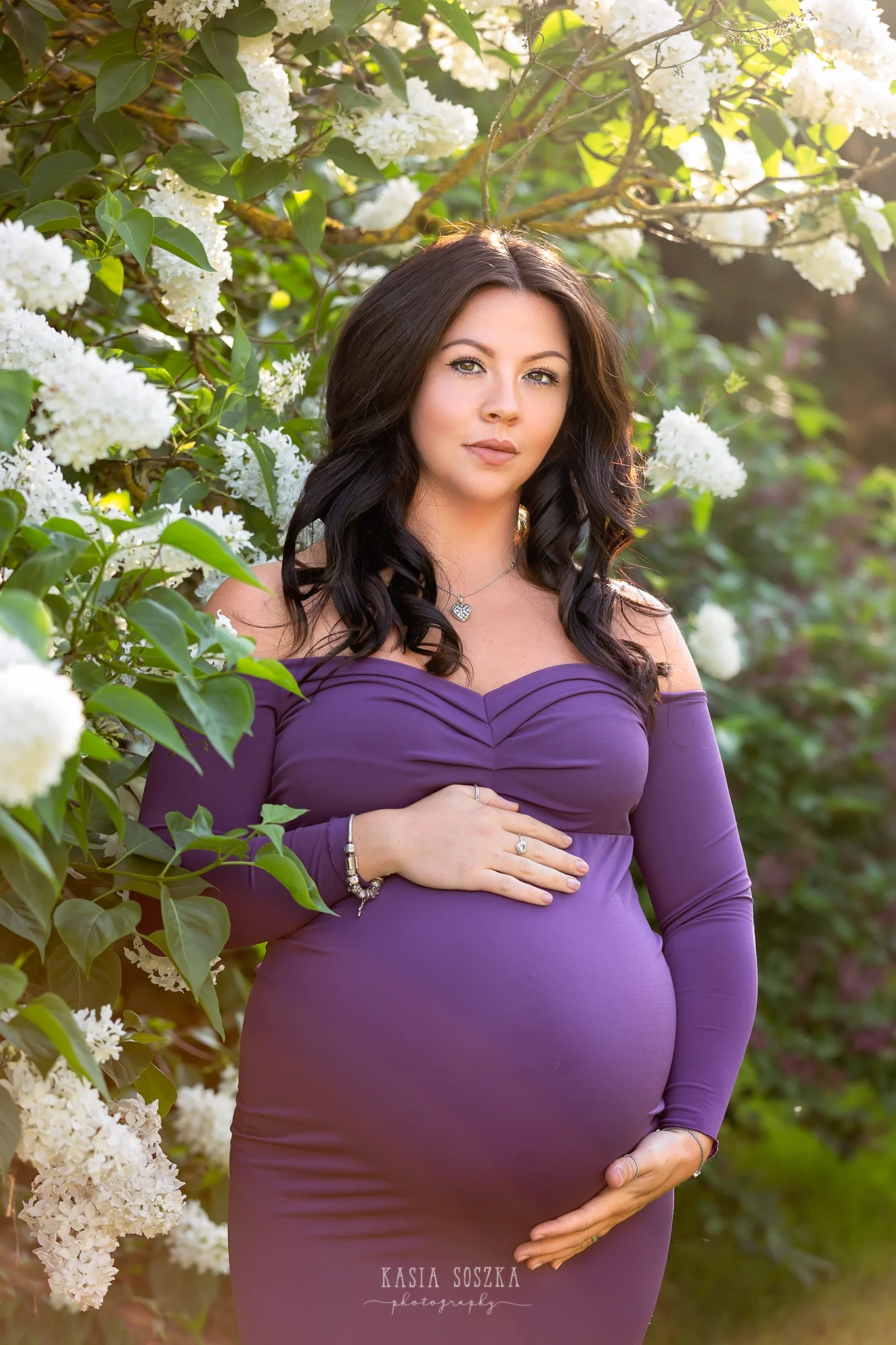 Leeds maternity photography Leeds Bradford York Harrogate maternity photographer:stunning pregnant woman in a long purple dress posing for a maternity photo around white lilac bush