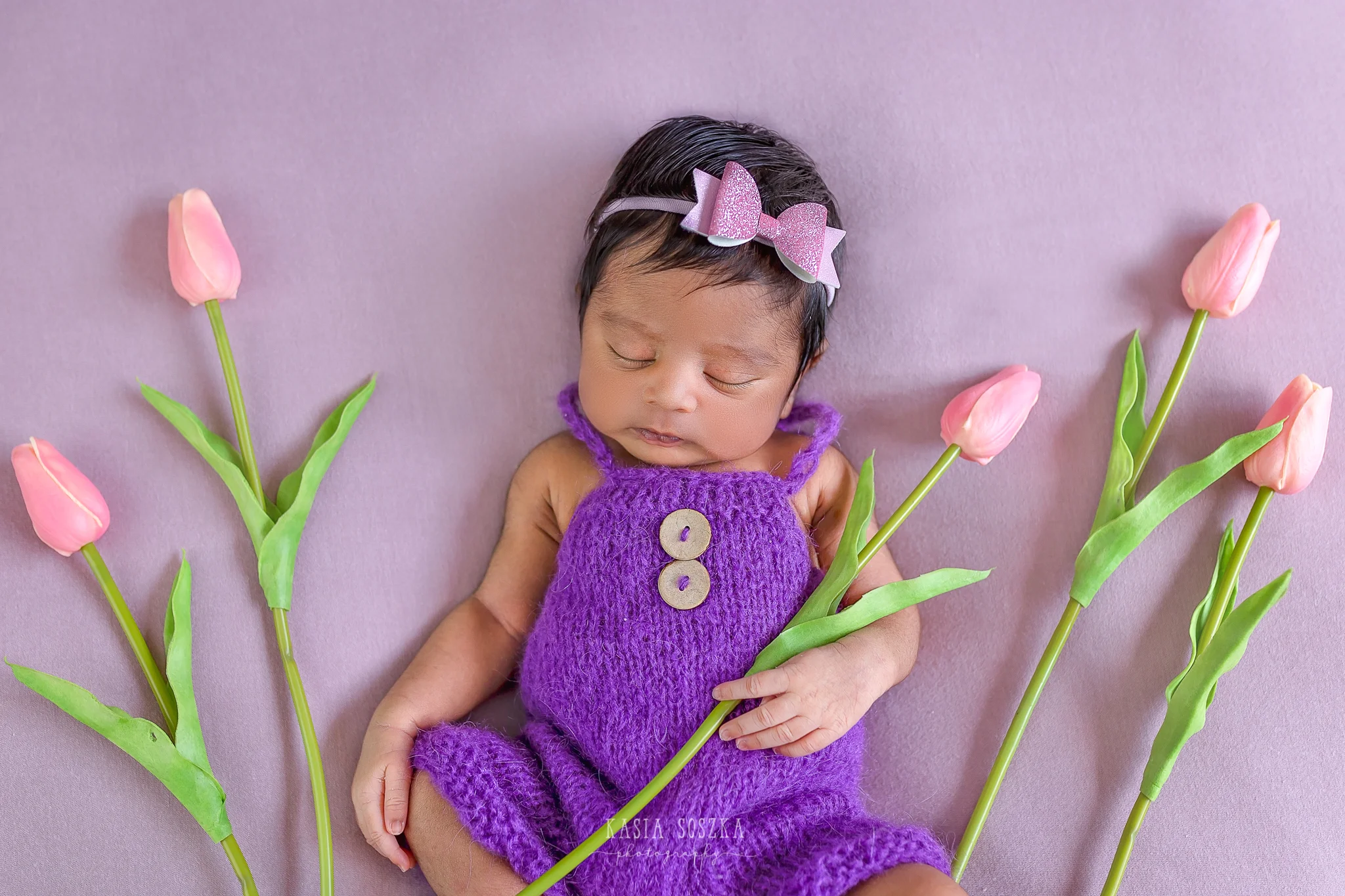 Newborn photography Leeds-Bradford-York-Harrogate: newborn baby girl wearing purple outfit on a pink blankets surrounded by pink tulips