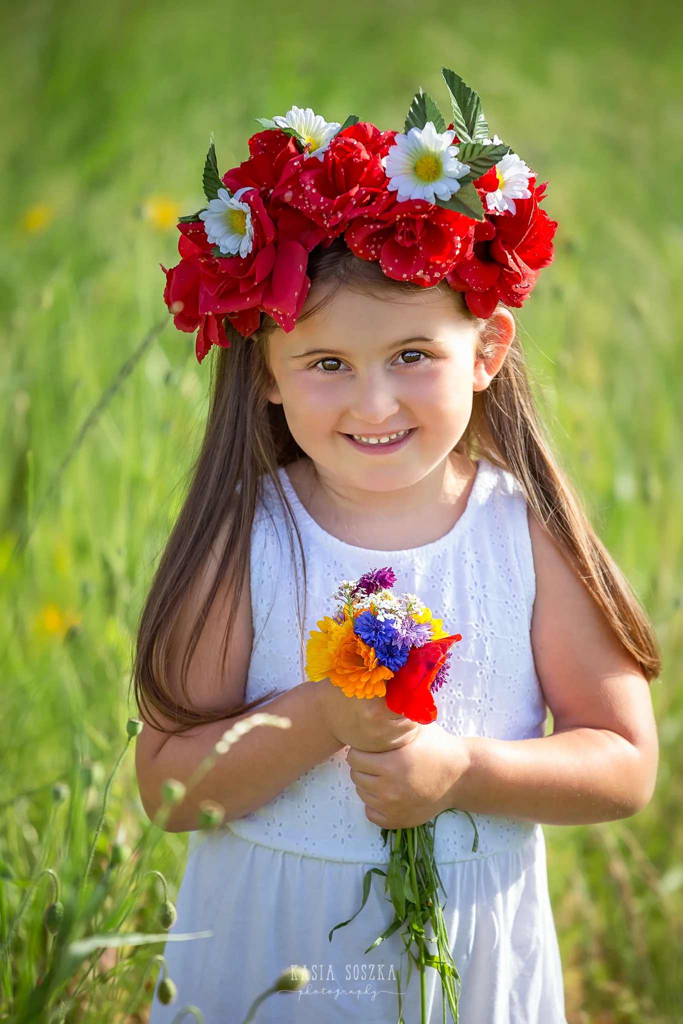 Children photography Leeds, child outdoor summer session Yorkshire: happy little girl standing in the middle of a summer meadow and holding a bunch of wildflowers.