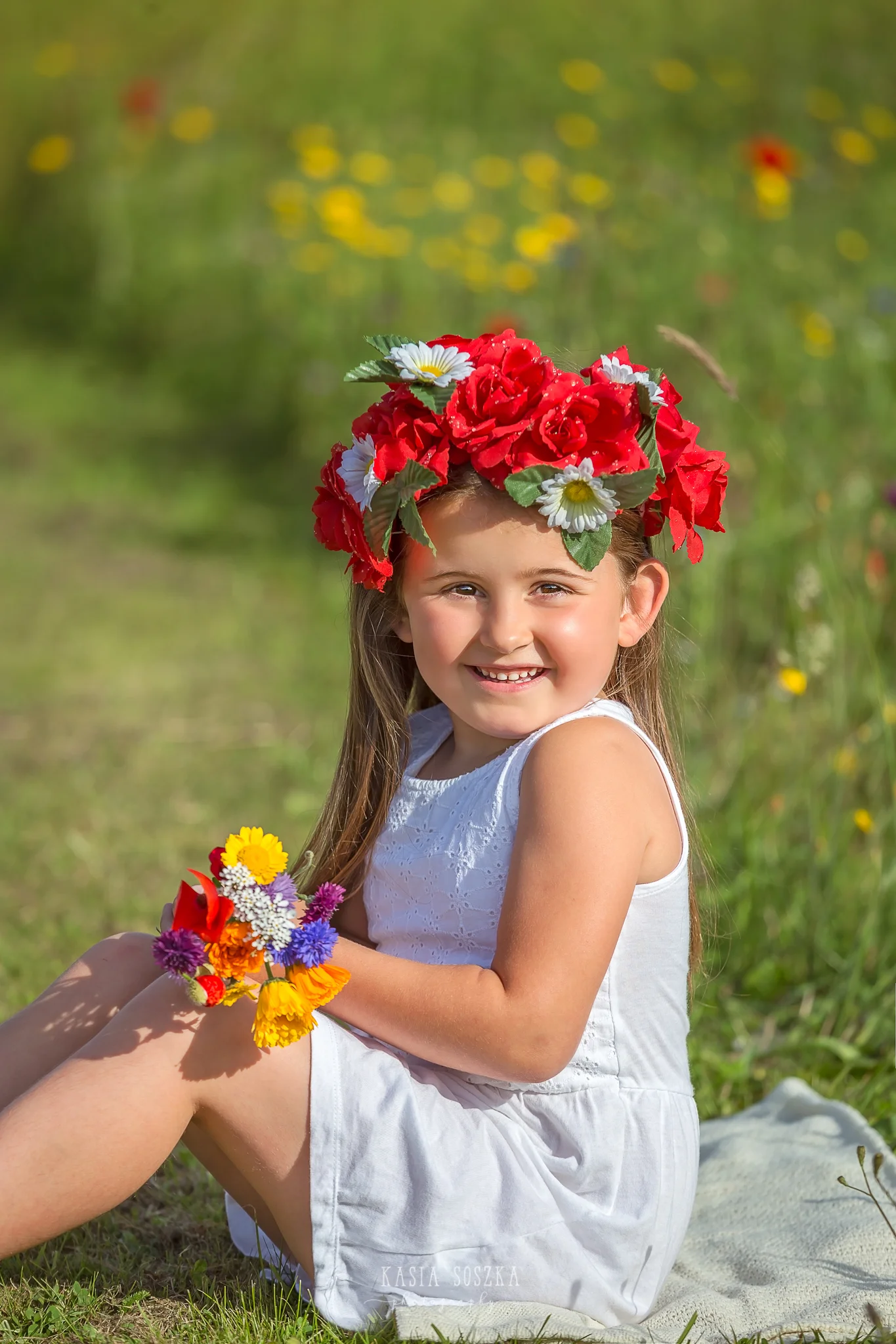 Children photography Leeds, child outdoor summer session Yorkshire: happy little girl sitting in a meadow and holding a bunch of wildflowers.