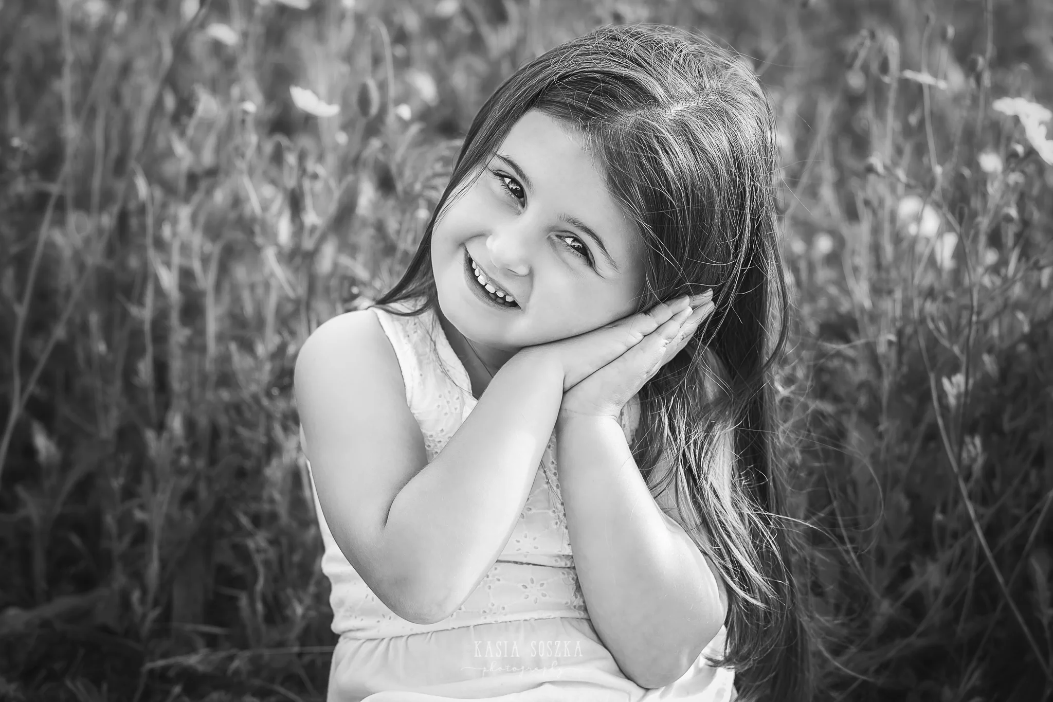 Children photography Leeds, child outdoor summer session Yorkshire: happy little girl sitting in a meadow and holding a bunch of wildflowers.