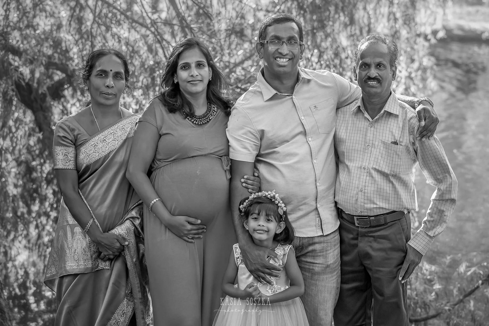 Family photography Leeds, maternity photography Leeds: expecting parents, their daughter and grandparents posing for a family photo by a lake