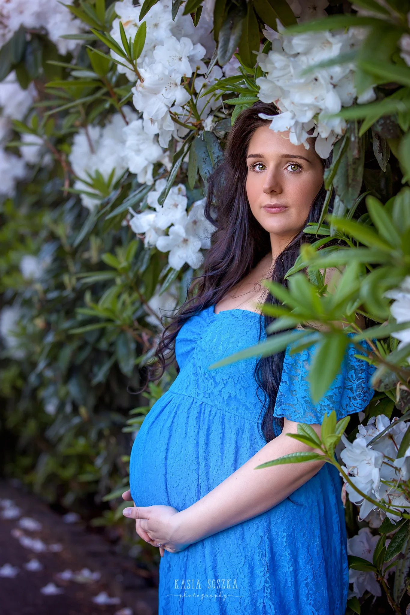Maternity photography Leeds, Yorkshire, pregnancy session Leeds: beautiful pregnant woman with long black hair standing against a wall of flowers