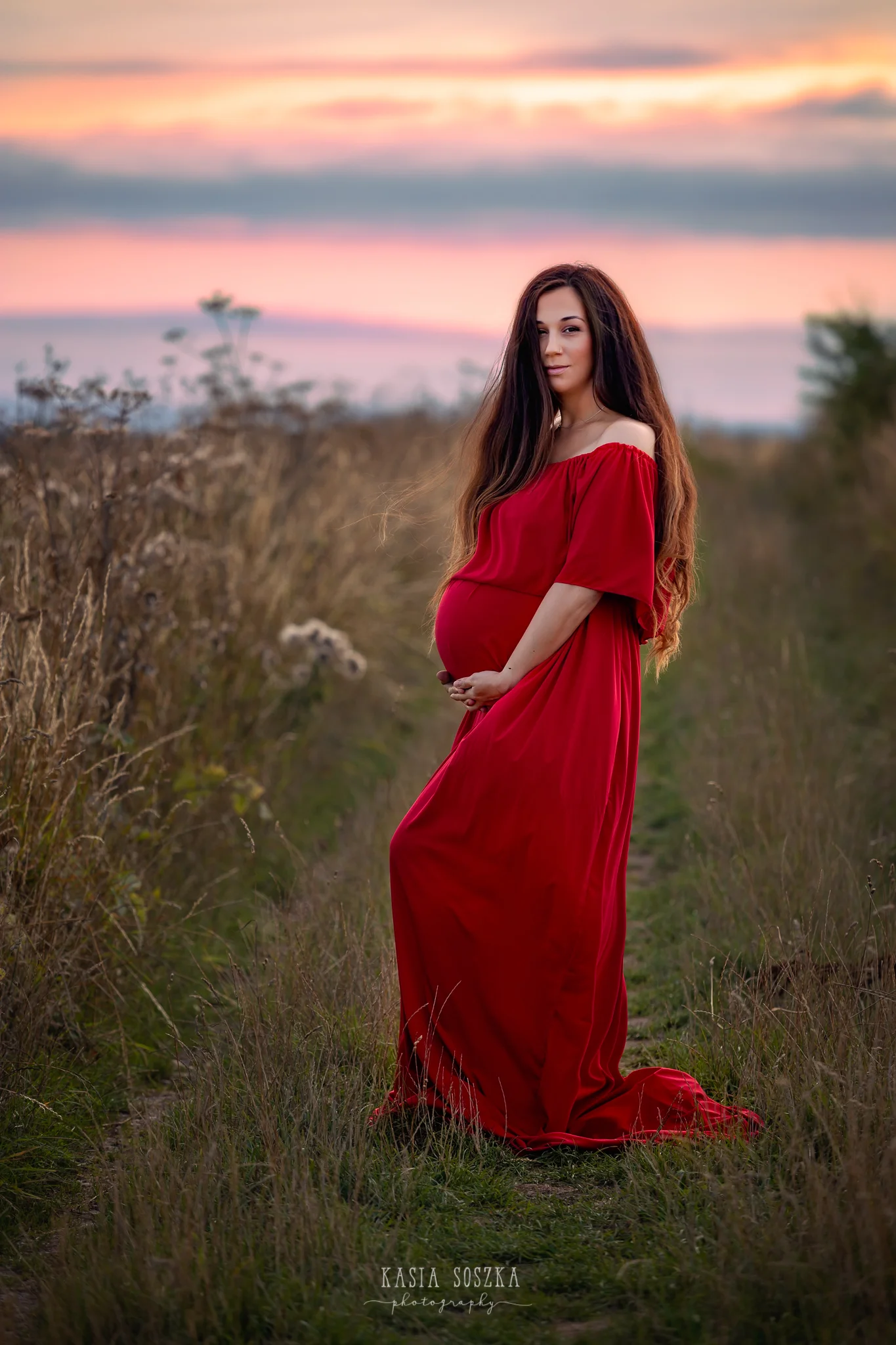 Maternity photography Yorkshire Leeds, Bradford, York, Harrogate, Wakefield: beautiful pregnant woman in red dress against the sunset in the countryside