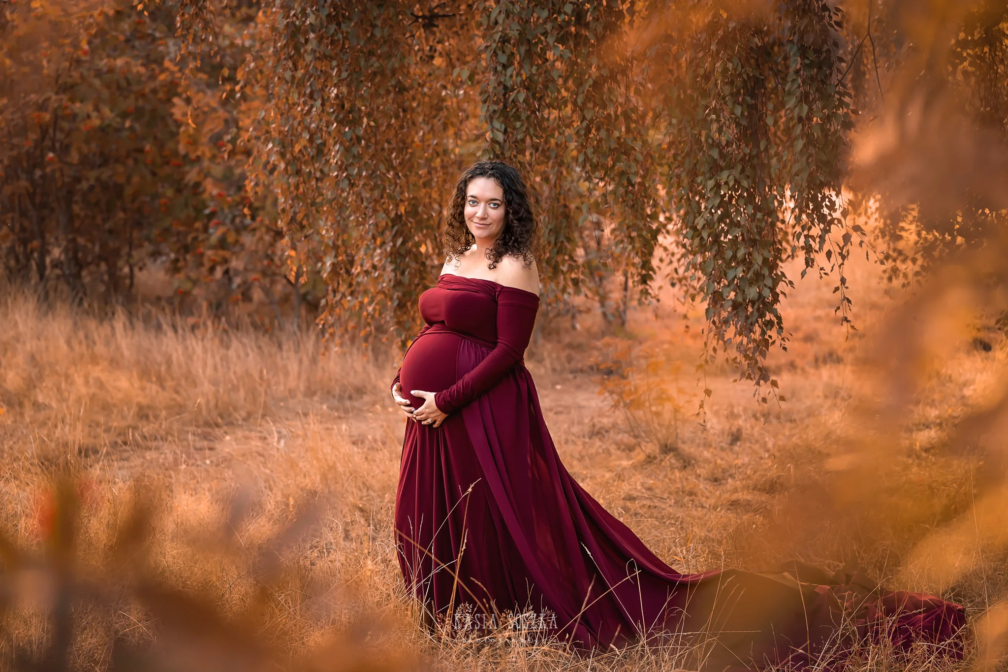Maternity photography, maternity photographer Leeds , York, Harrogate, Bradford: woman in a long wine red dress posing for her pregnancy photos in a park in Leeds, Yorkshire, on a sunny autumn day