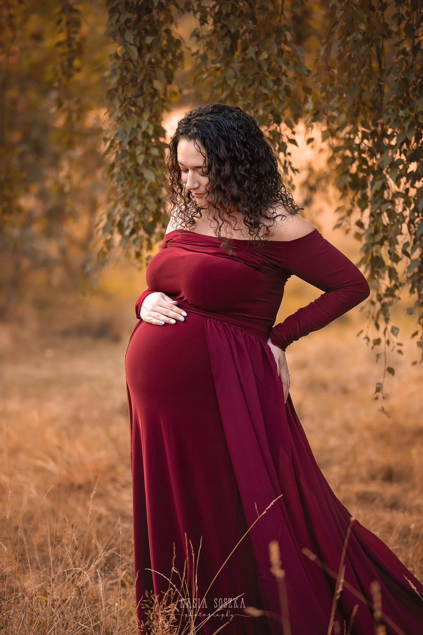 Maternity photography, maternity photographer Leeds , York, Harrogate, Bradford: woman in a long wine red dress posing for her pregnancy photos in a park in Leeds, Yorkshire, on a sunny autumn day