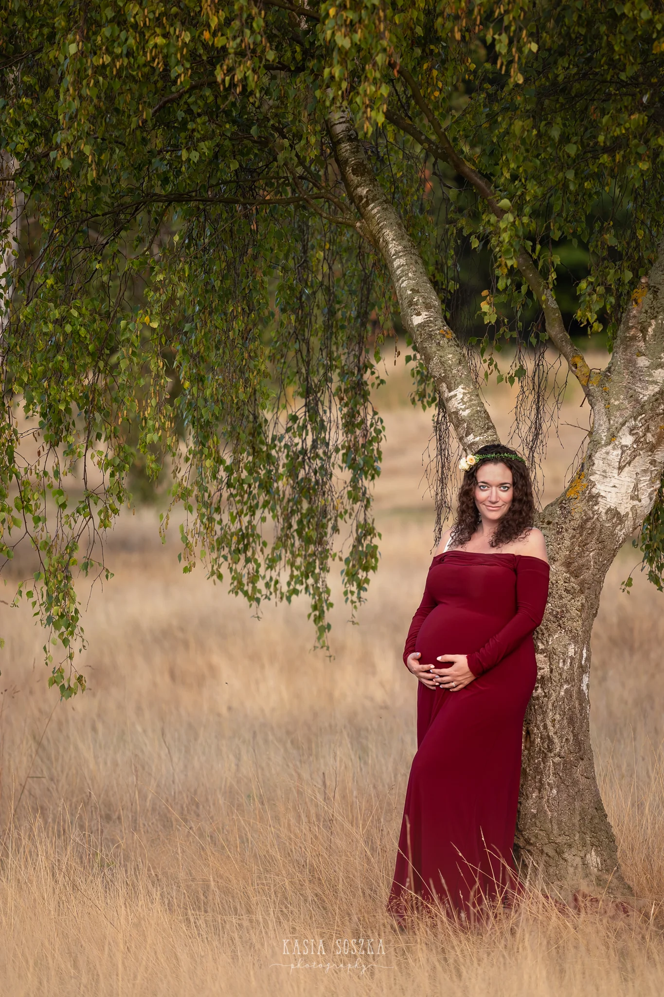 Maternity photography, maternity photographer Leeds , York, Harrogate, Bradford: woman in a long wine red dress posing for her pregnancy photos in a park in Leeds, Yorkshire, on a sunny autumn day