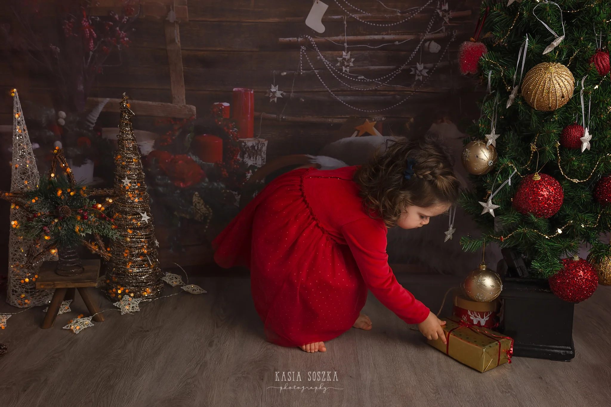 Child photographer Leeds, York, Bradford, Harrogate. Christmas Mini Sessions 2018 Leeds: beautiful little girl in a red dress checking presents under the Christmas tree.