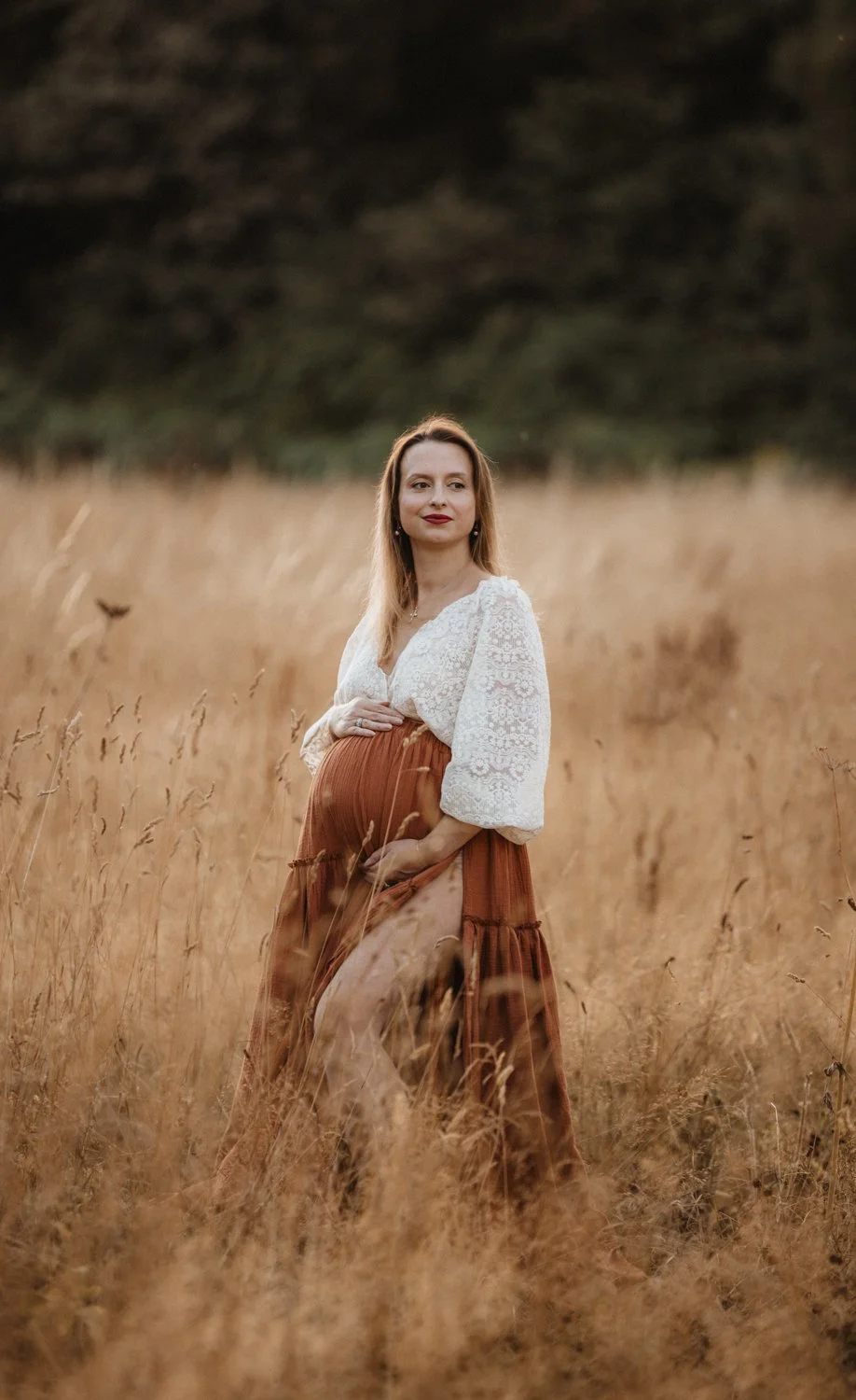 A boho style outdoor maternity photoshoot: pregnant woman in a rust skirt and a lace top standing in a summer meadow during her maternity shoot in Leeds, Yorkshire