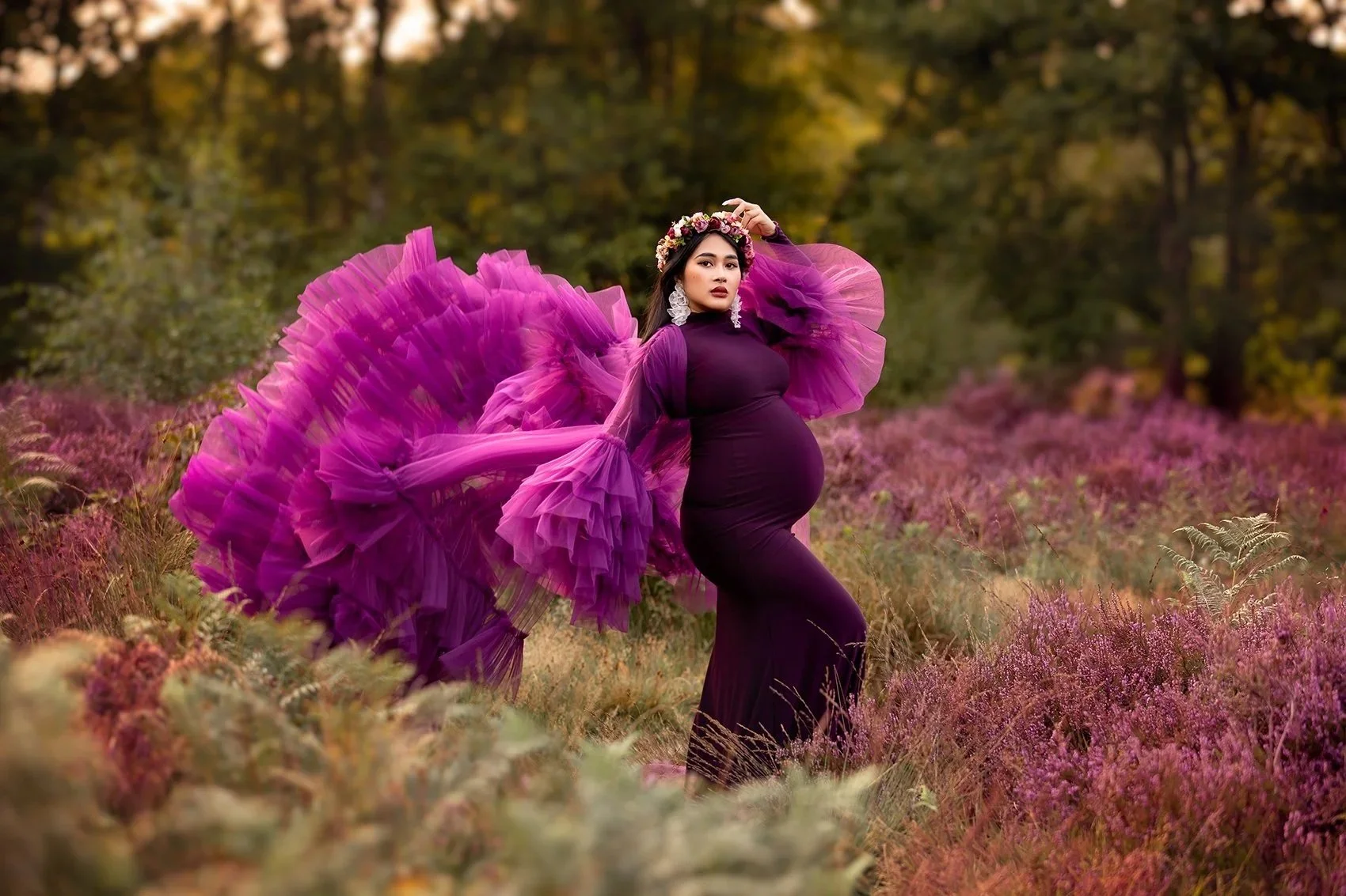 Stunning pregnant woman in a purple flowy couture maternity gown posing for a photo surrounded by purple heather during her maternity session in Leeds  