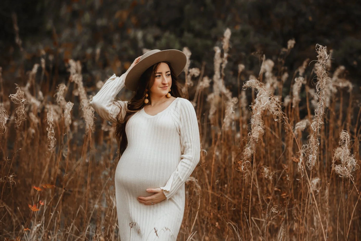 Pregnant woman in a cream sweater dress and a fedora hat during her autumn maternity photoshoot in Leeds, Yorkshire