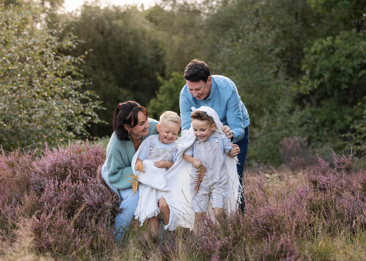 Mum and dad wrapping their 2 little boys in a blanket, all laughing, during their family photoshoot in Leeds