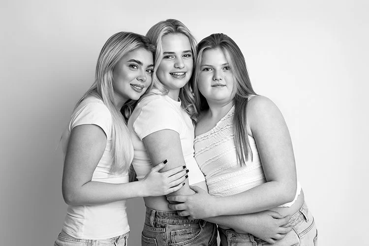 Black & white portrait of 3 young sisters hugging each other