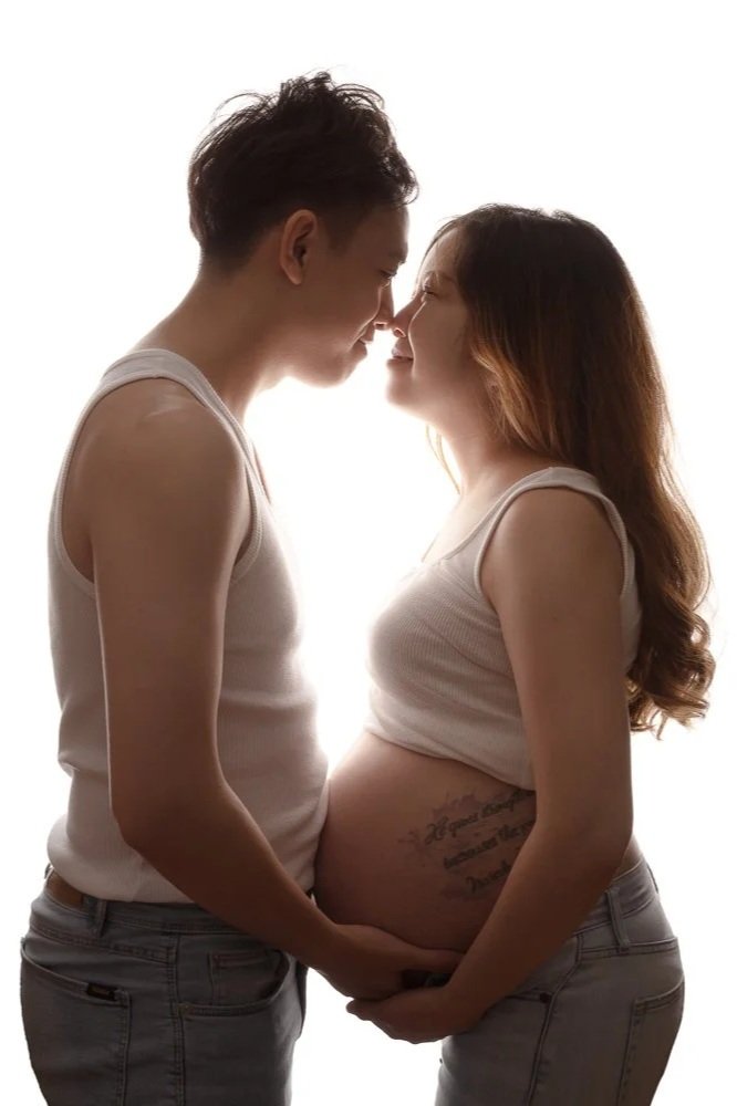 A cute young couple wearing white shirts and jeans looking at each other and rouching noses during their natural and casual maternity shoot in Leeds