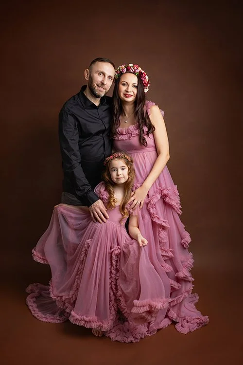A family photo of mum, dad and daughter. Mum and daughter are dressed in matching pink desses