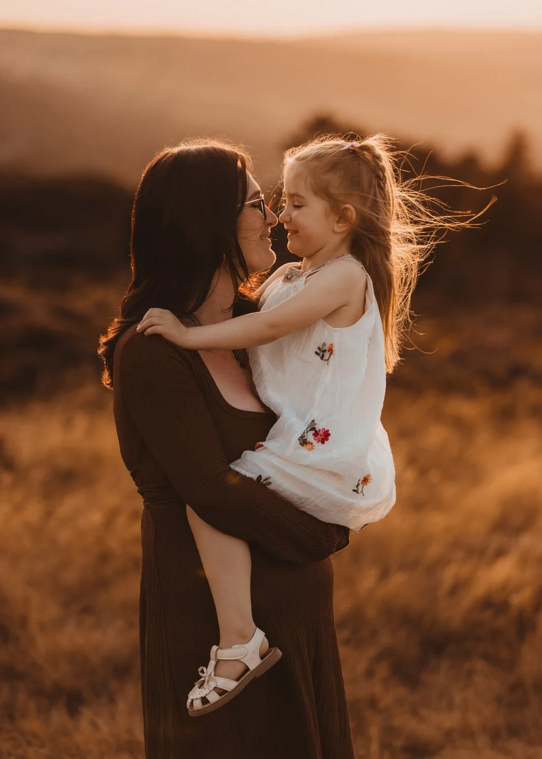 Mum holding her little daughter, both smiling and looking at each other, with setting sun behind them, during their family shoot on Ilkley Moor with Kasia Soszka Photography