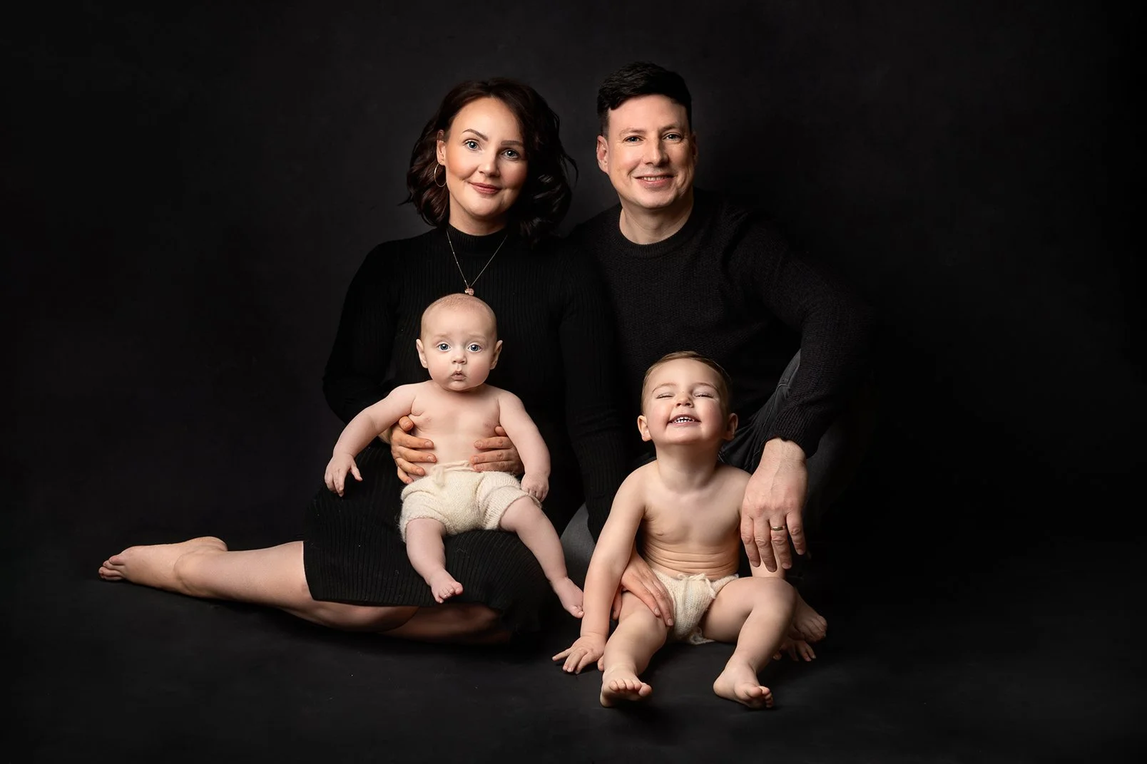 A family portrait of a mum and dad dressed in black and their 2 little sons