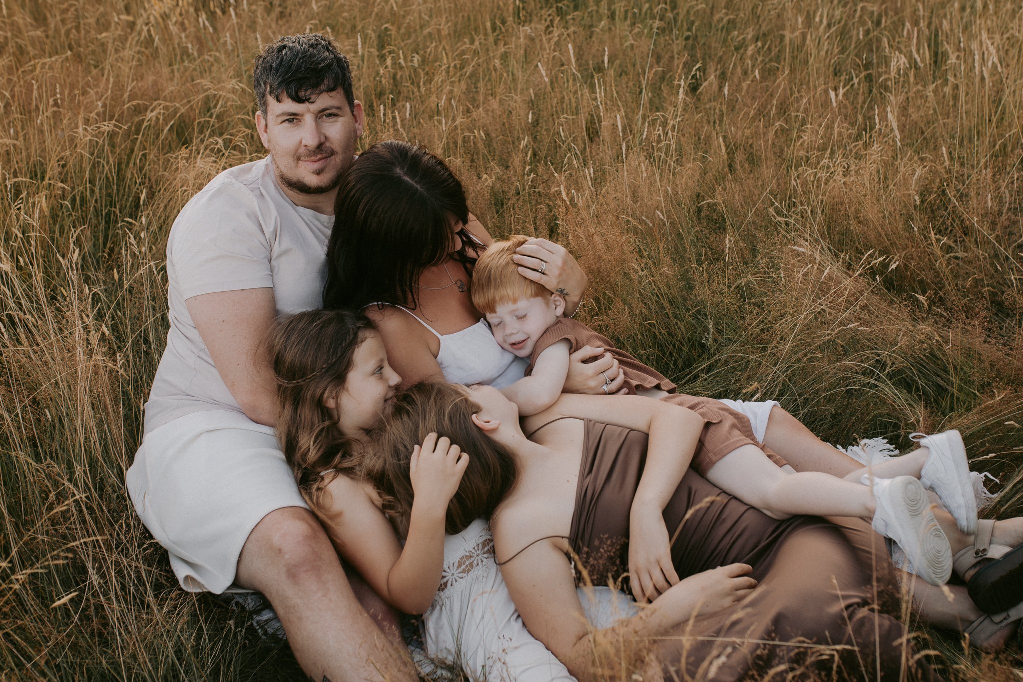 Mum, dad and their 3 children cuddling up on a blanket, in a summer meadow during their family photoshoot in Leeds