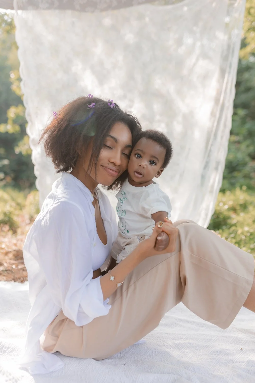 A young mother sitting on a blanket and hugging her baby son