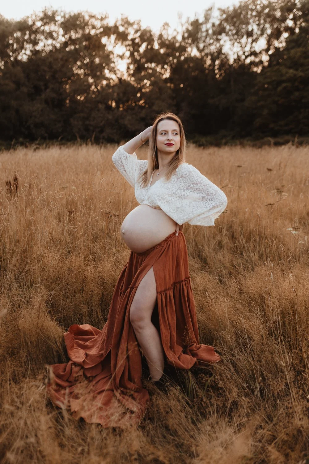 Pregnant woman in a boho skirt and lace top set standing in a summer meadow  during her maternity photoshoot in Leeds