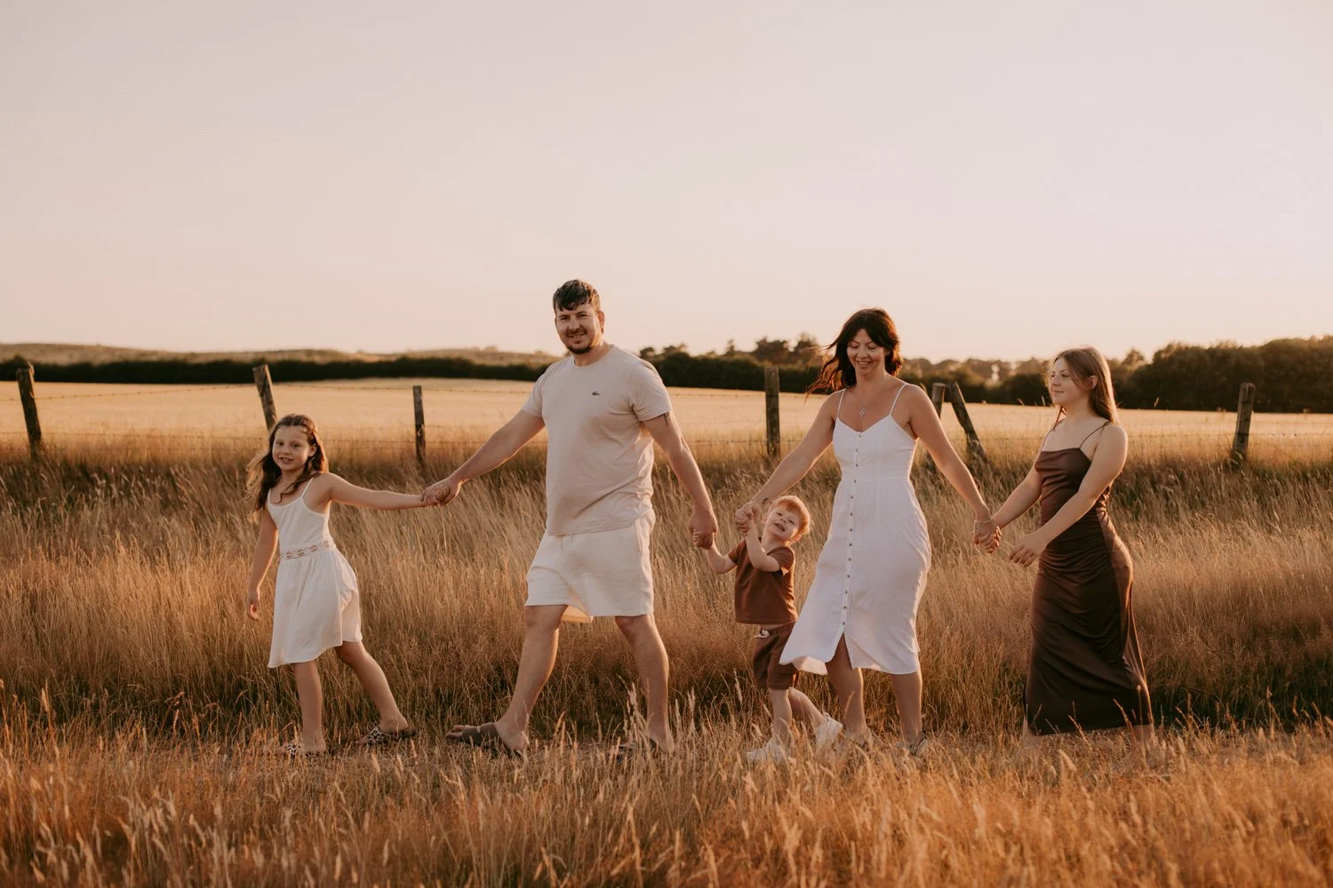 Mum, dad and their 3 children holding hands and walking through a summer field during golden hour photoshoot in Leeds