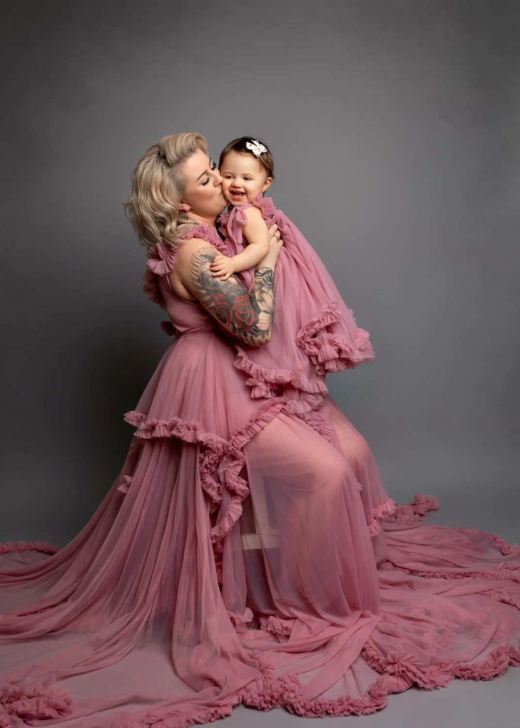 Mum in a couture pink gown kissing her baby daughter, who is dressed in a matching pink dress, during their family photoshoot in Leeds