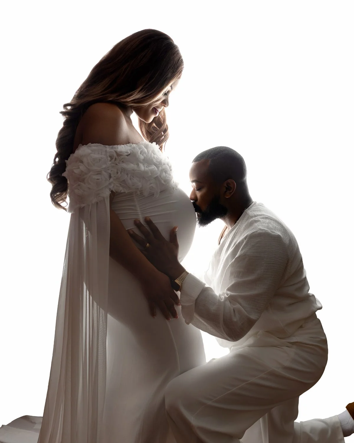 A man kissing his pregnant wife's belly during their maternity photoshoot in Leeds. Both are dressed in white. a Backlit portrait.