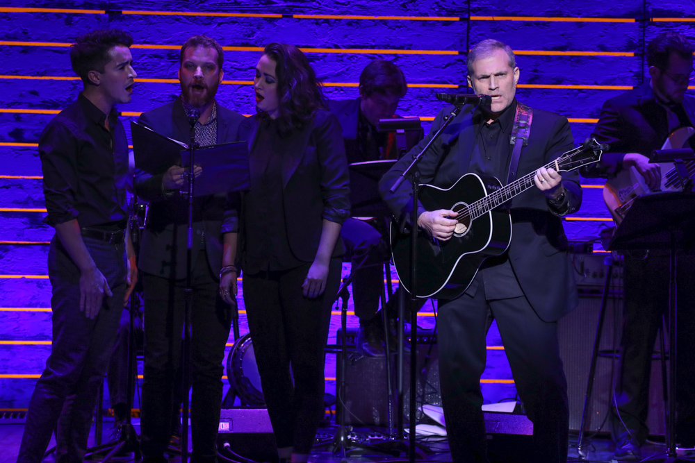 Broadway theatre performer singing and playing guitar on stage