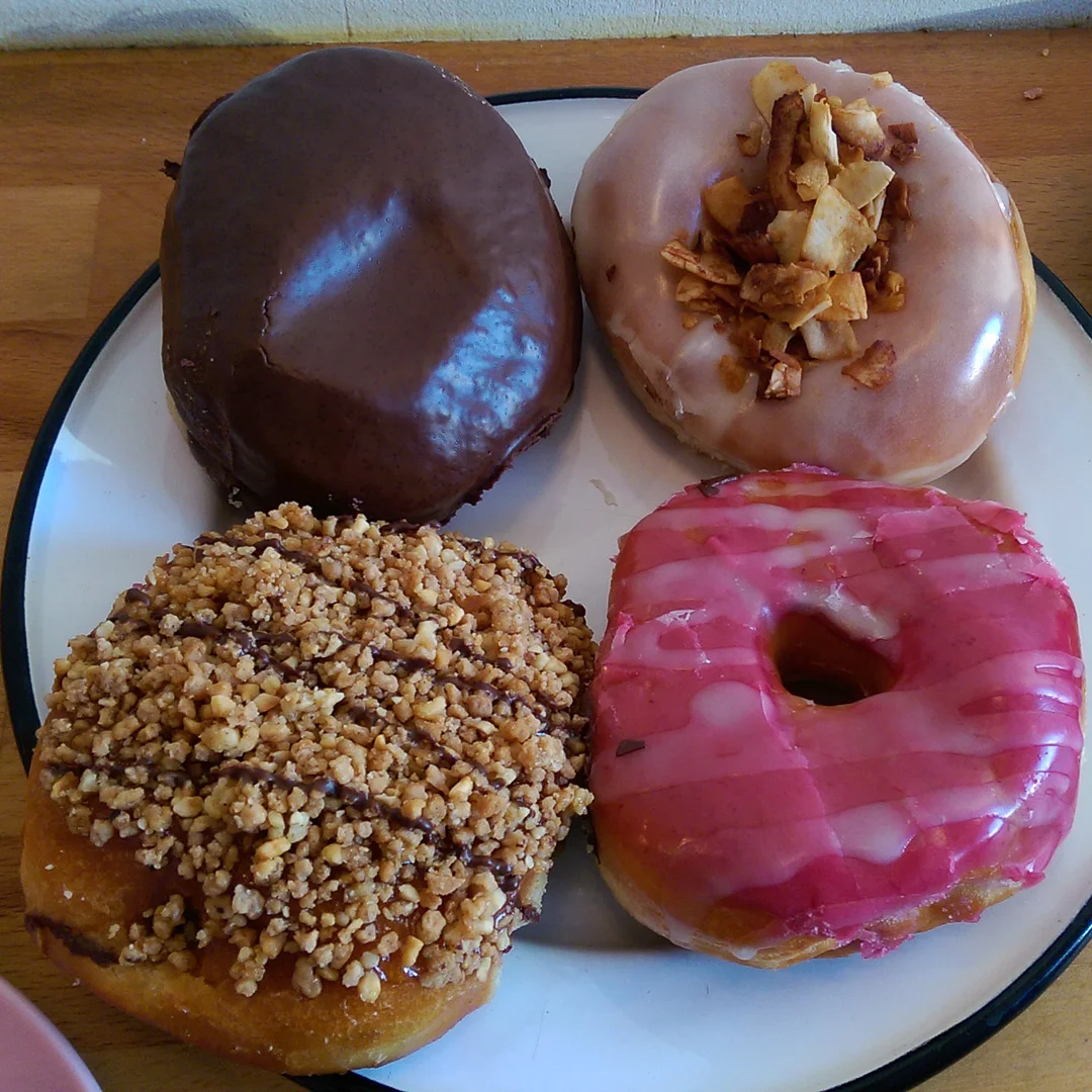 Starting from the top left and going clockwise: Boston Cream, Maple frosted with Coconut Bacon, Nutella filled, and Raspberry frosted—all of this delciousness is vegan!
