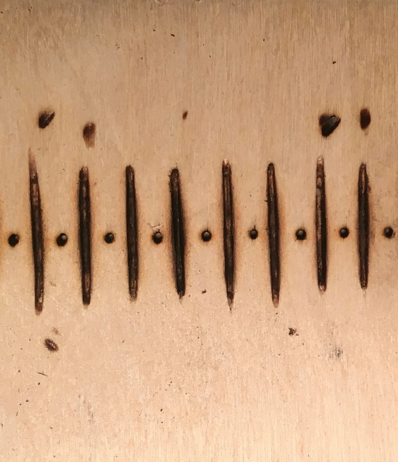 Image: Dots and dashes cut and burned into wood to create a loom's heddle