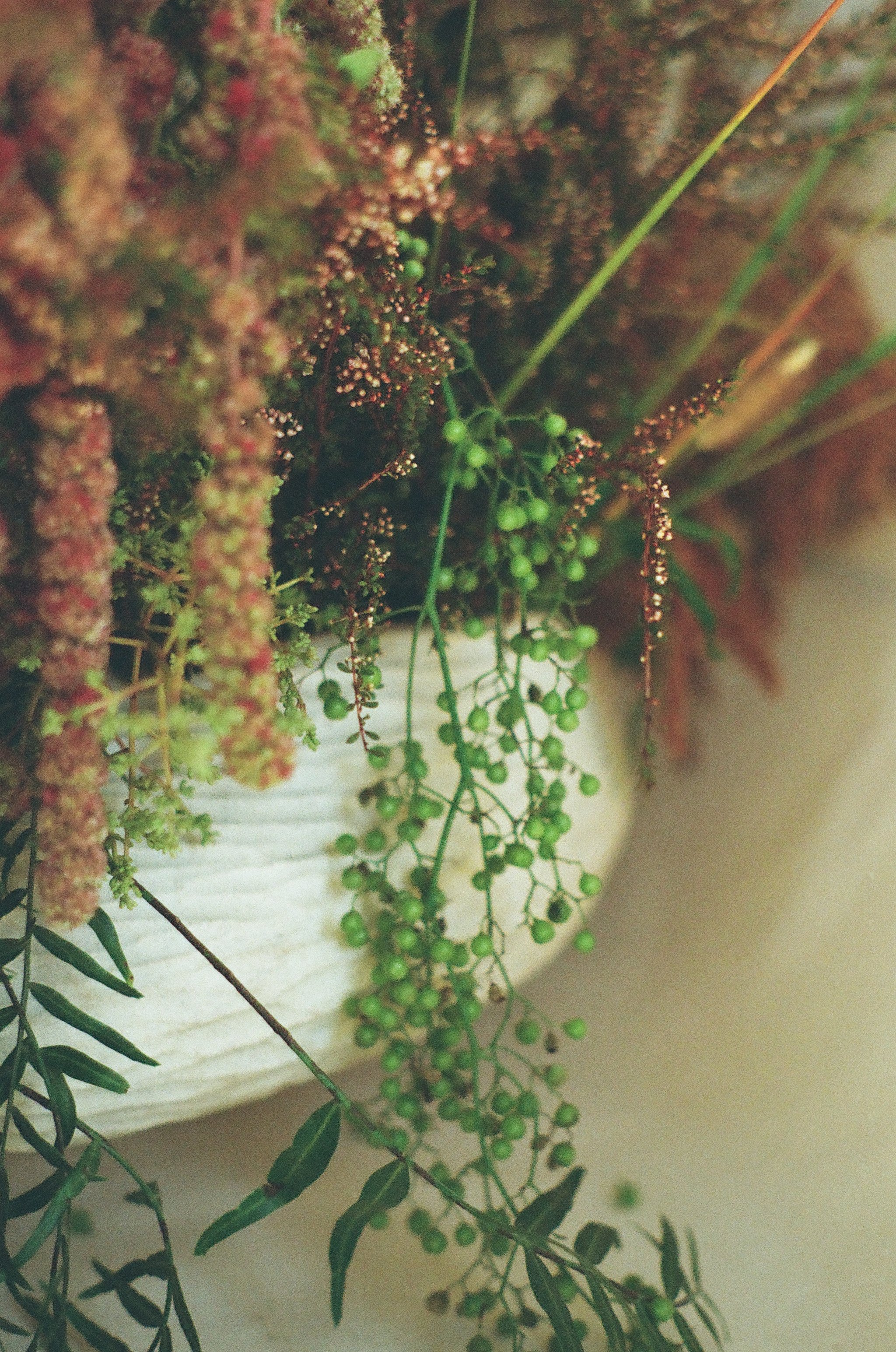 A close up image of a green and pink floral and leaf arrangement inside a white handmade ceramic bowl with a carved wavy surface texture.