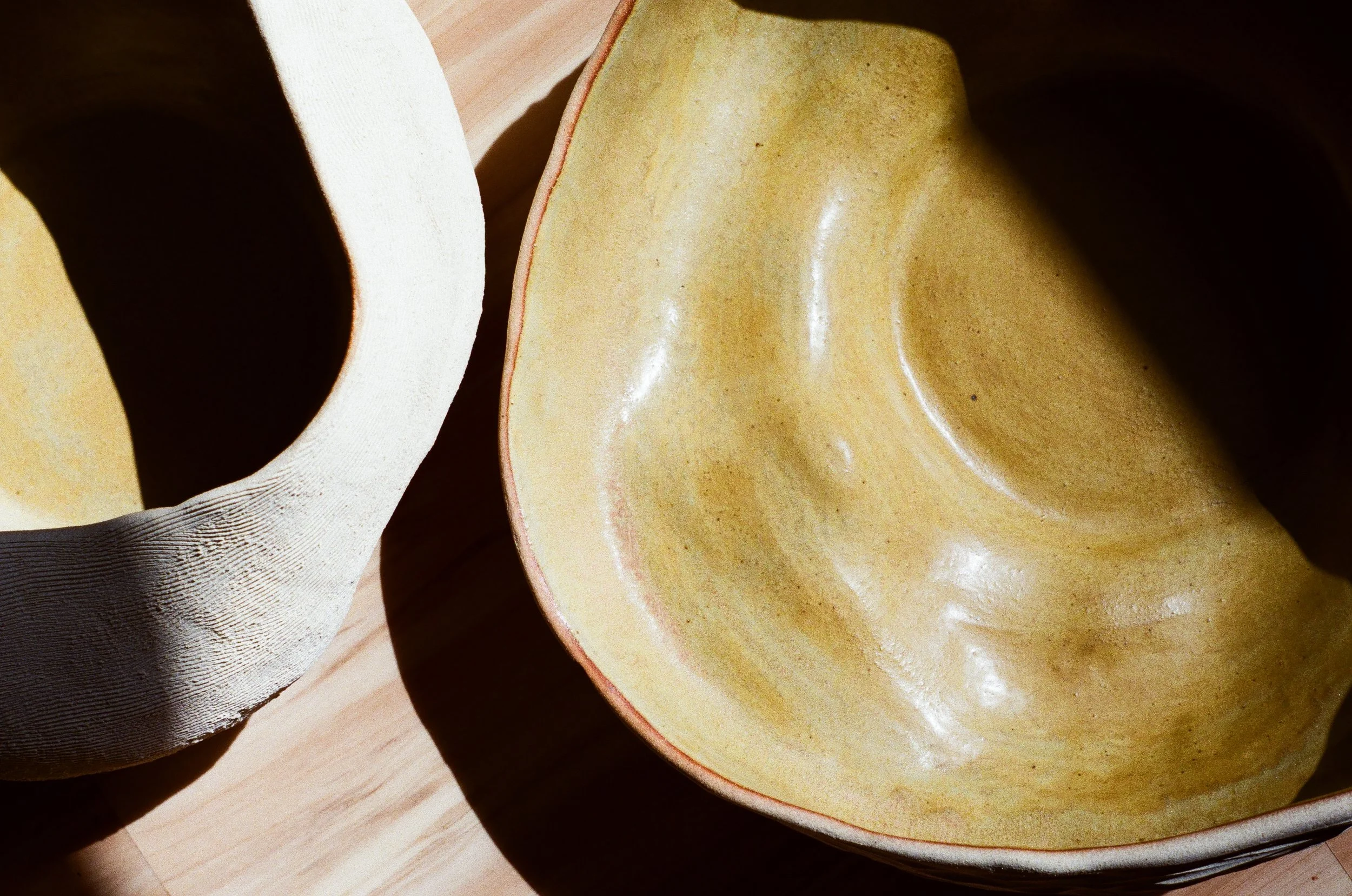 A view from above of two handmade ceramic bowls. The bowls are white on the outside with thin lines and cross hatches that make up the textured surface. The insides are glazed with a semi-shiny light yellow green glaze.